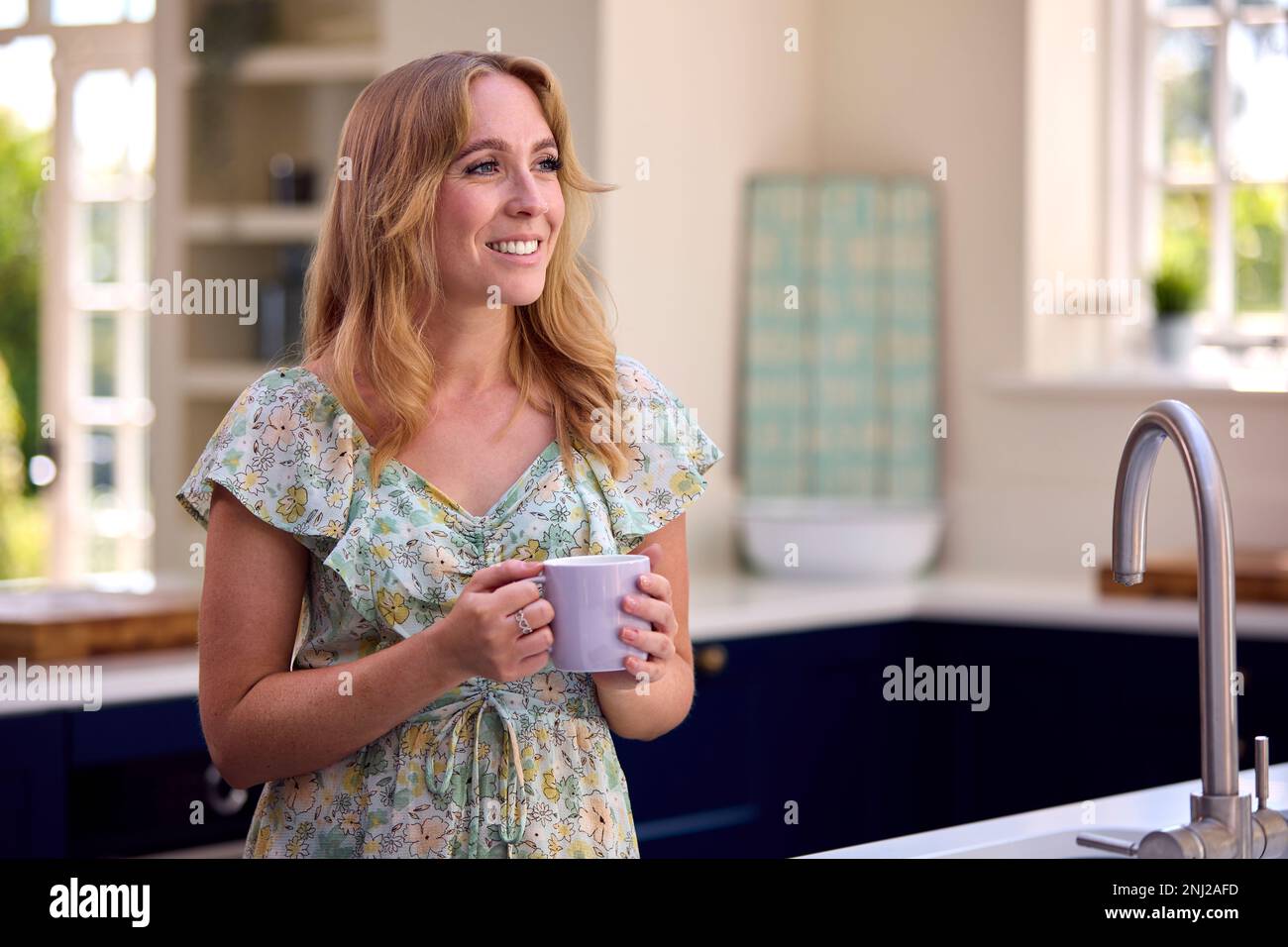 Lächelnde Frau, Die In Der Küche Steht Und Sich Mit Einer Tasse Kaffee Entspannt Stockfoto