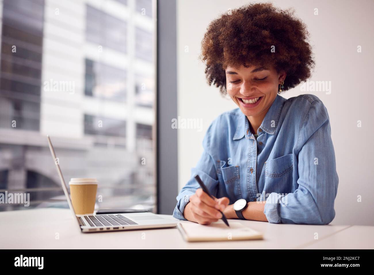Junge Geschäftsfrau Im Modernen Büro, Die An Einem Notebook Arbeitet Und Notizen In Notebook Macht Stockfoto