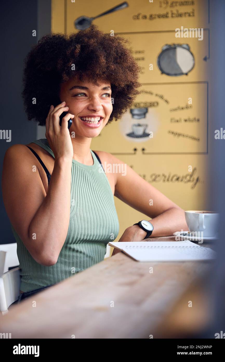 Weibliche Kundin Im Coffee Shop, Die Am Fenster Arbeitet Und Mit Dem Handy Spricht Stockfoto