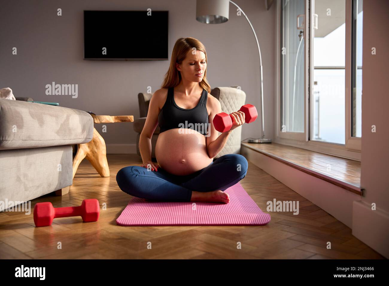 Schwangere Frau Trägt Fitnesskleidung Auf Der Matte Zu Hause Beim Training Mit Gewichten Stockfoto