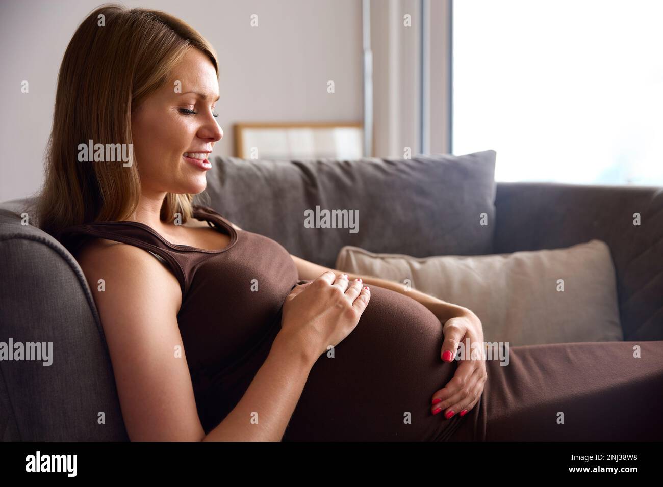 Schwangere Frau, Die Sich Auf Dem Sofa Im Home Holding Bauch Entspannt Stockfoto