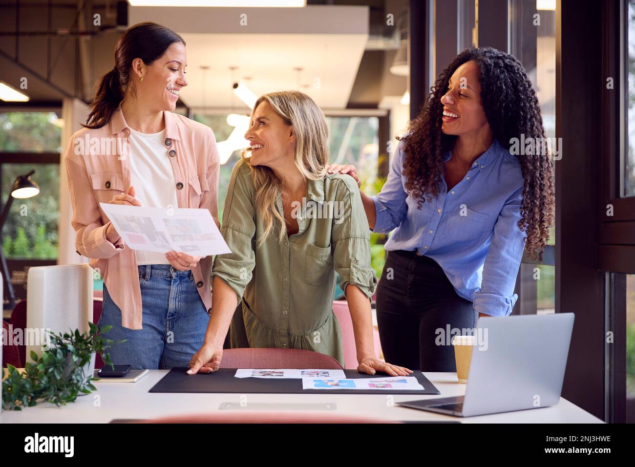 Weibliches Business-Team Steht Am Schreibtisch Im Großraumbüro Und Genehmigt Die Prüfung Von Proofs Oder Design-Layouts Stockfoto