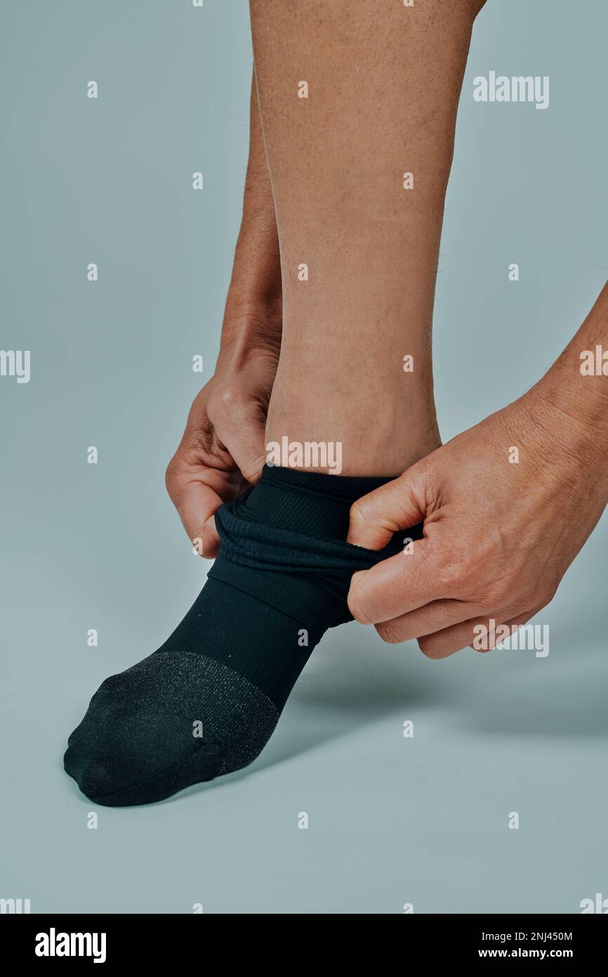 Ein Mann zieht gerade eine Kompressionssocke vor einem cremefarbenen Hintergrund an Stockfoto