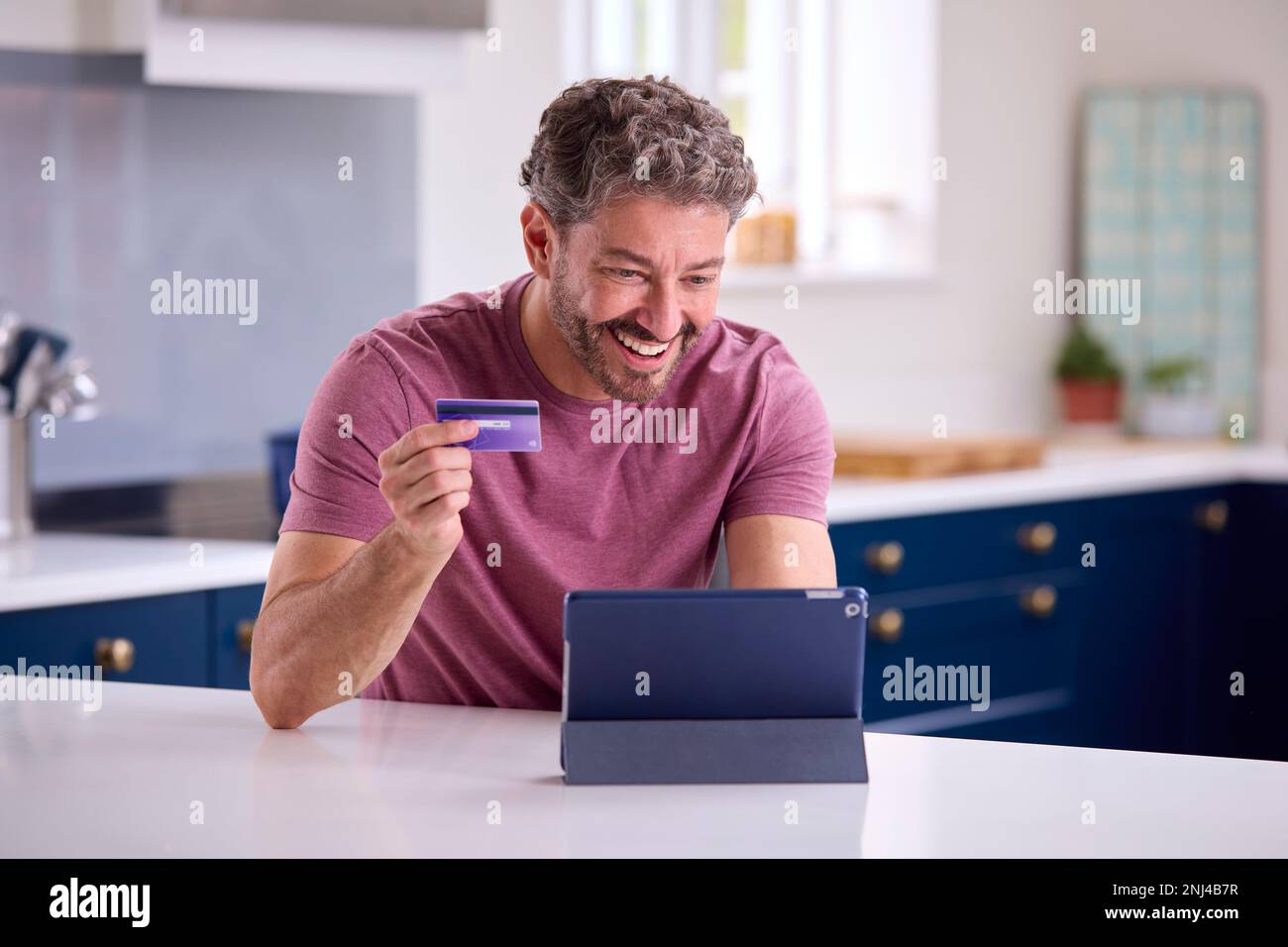 Reifer Mann Mit Kreditkarte, Der Zu Hause Ein Digitales Tablet Verwendet, Um Urlaub Zu Buchen Oder Einzukaufen Stockfoto