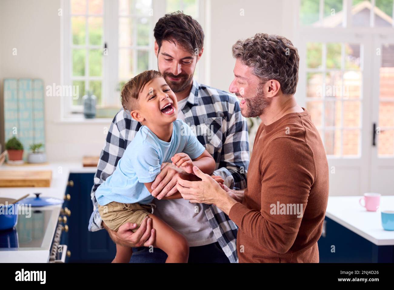 Same-Sex-Familie Mit Zwei Vätern, Die In Der Küche Kochen, Mit Sohn, Der An Der Theke Sitzt Stockfoto