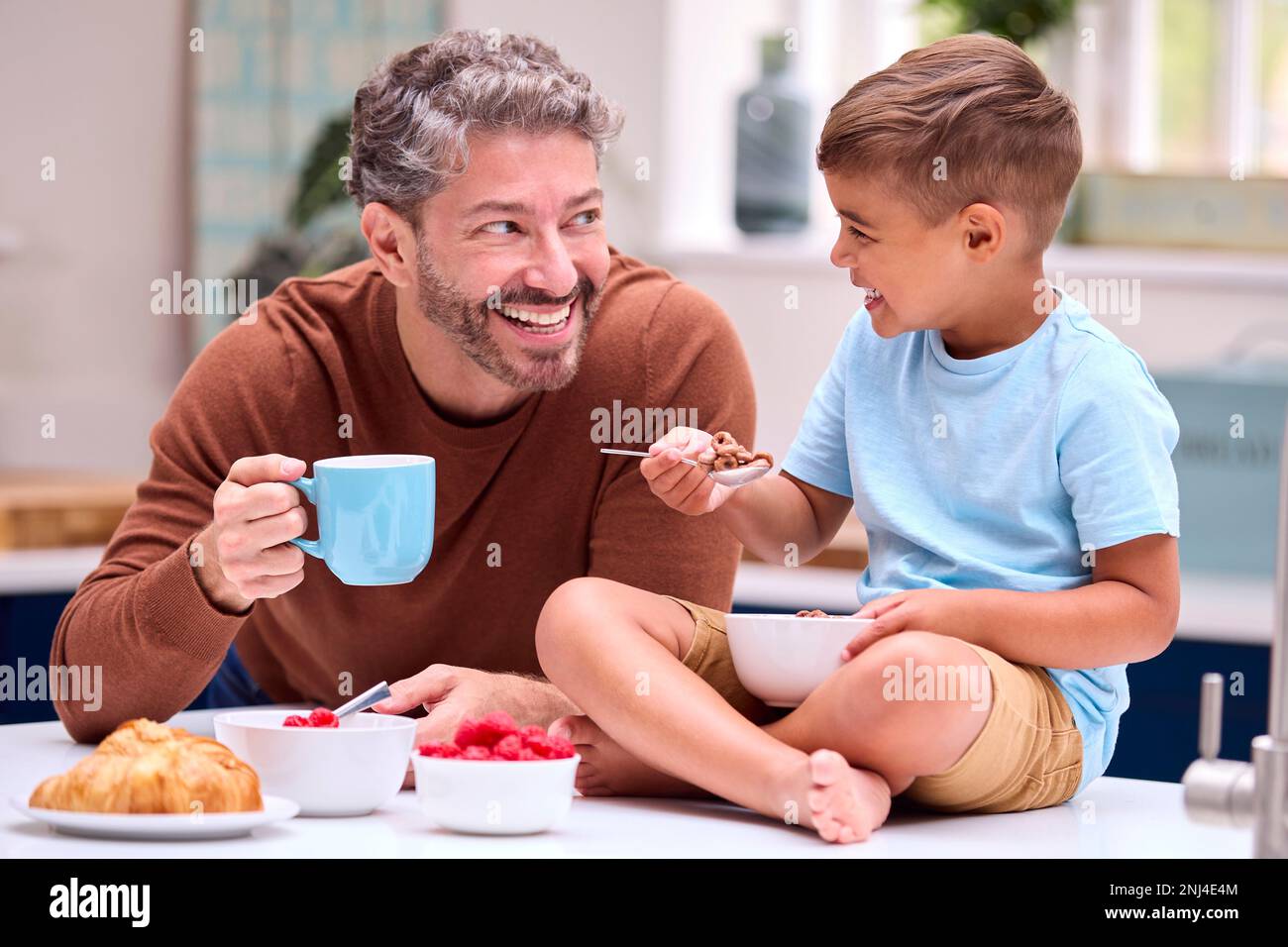 Familie Mit Vater In Der Küche, Sohn Sitzt An Der Theke Und Frühstückt Zusammen Stockfoto