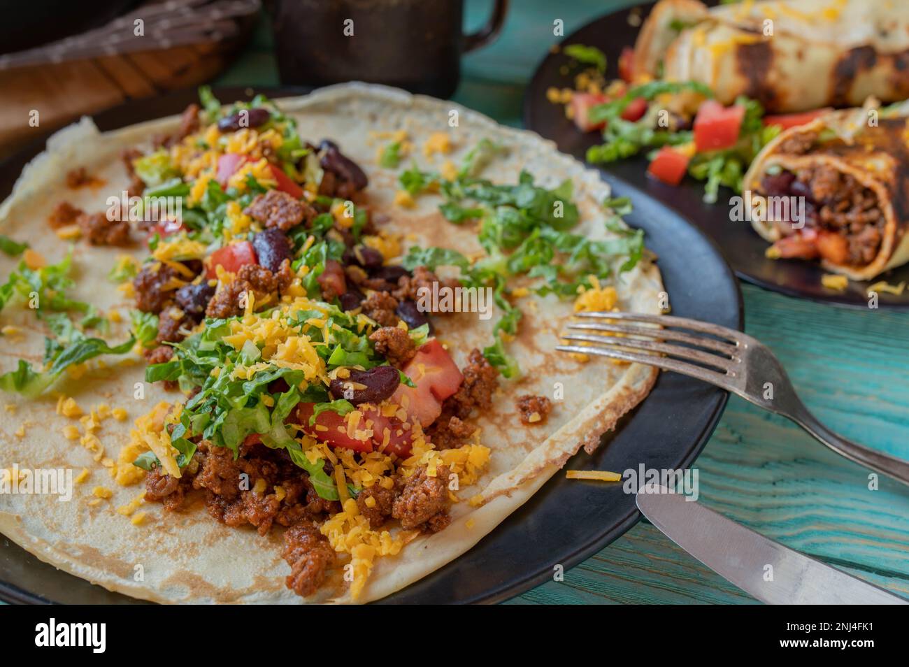 Offener Burrito mit Rinderhack, Kidney Beans, Cheddar Cheese, Tomaten und Salat auf einem Teller Stockfoto