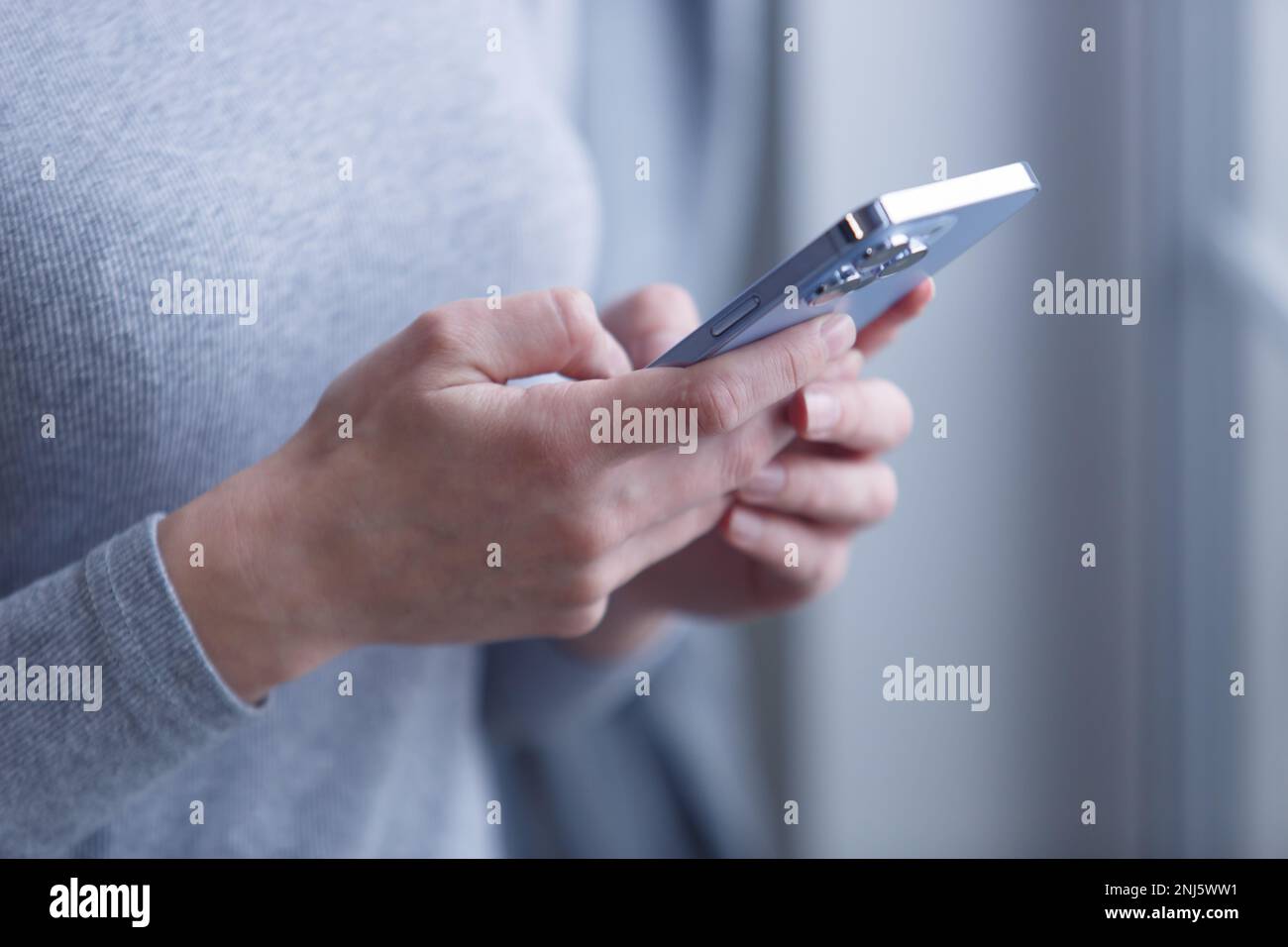 Junge Frau, die eine Nachricht auf einem modernen blauen Smartphone tippt. Nahaufnahme einer Frau, die ein Mobiltelefon in der Hand hält, mit Dreifachkamera Stockfoto