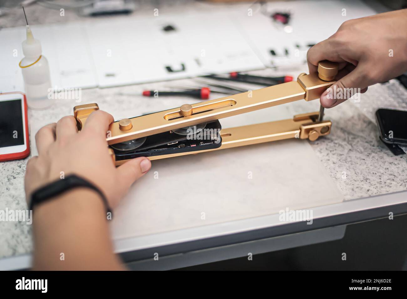 Draufsicht des Arbeitsplatzes, Nahaufnahme. Ein Techniker arbeitet mit einem Smartphone-Reparatur- und Wartungswerkzeug in einer Elektronikwerkstatt Stockfoto