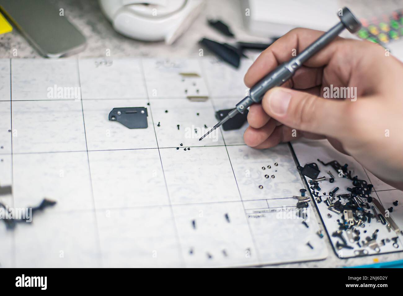 Draufsicht des Arbeitsplatzes, Nahaufnahme. Der Techniker zerlegt das Smartphone in einer Elektronikwerkstatt mit einem Schraubendreher. Stockfoto