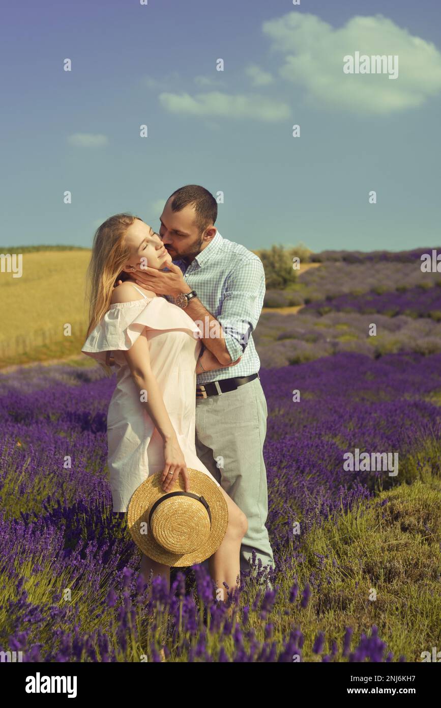 Ein verliebtes Paar küsst sich auf einem Lavendelfeld. Romantik und Reisen, Liebes. Ein hübsches Mädchen in einem Kleid und einem Strohhut und ein Mann. Stockfoto