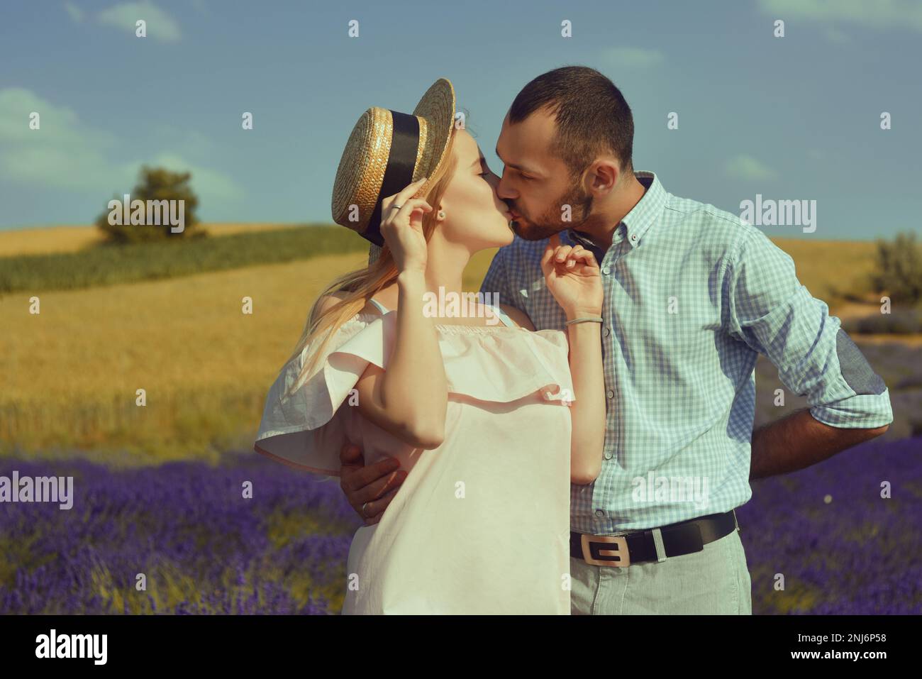 Ein verliebtes Paar küsst sich auf einem Lavendelfeld. Romantik und Reisen, Liebes. Ein hübsches Mädchen in einem Kleid und einem Strohhut und ein Mann. Stockfoto