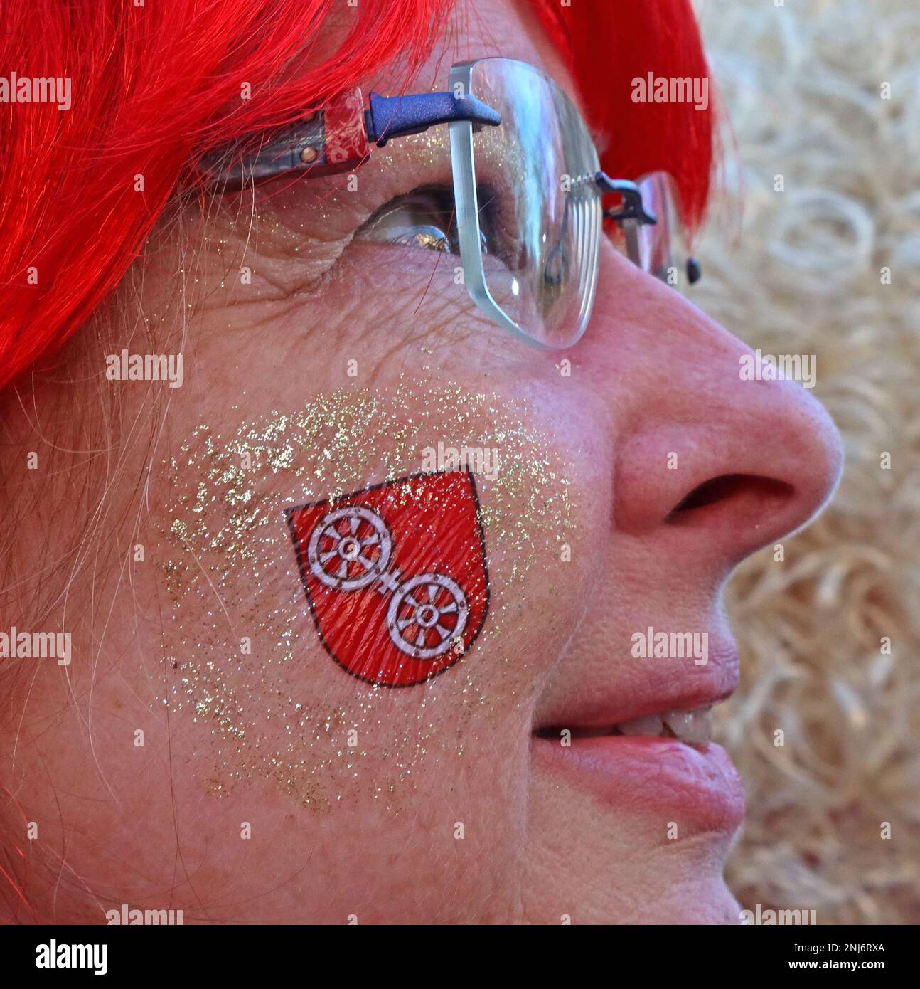 Lady genießt die Mainz Fastnacht, Shrove Monday, in einer roten Perücke mit temporärem Tattoo in Rot auf das Wappen der Stadt, Februar 2023 Stockfoto