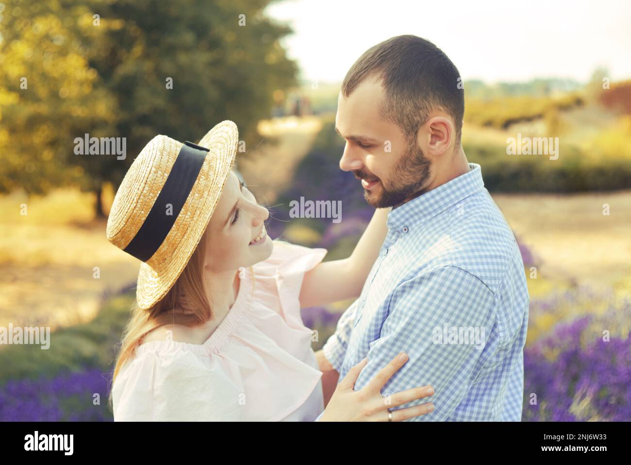 Ein verliebtes Paar auf einem Lavendelfeld bei Sonnenuntergang bei gutem Wetter. Schöne Frau in einem Kleid und Stroh panama mit einem Mann im Hintergrund der Natur, Stockfoto