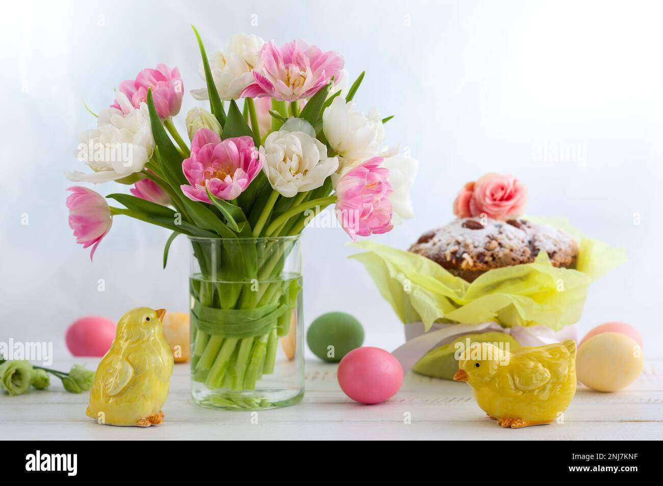 Osterstrauß mit Frühlings-Tulpen mit Osterkuchen, Eiern und festlicher Einrichtung auf weißem Holztisch. Osterkonzept mit Kopierraum. Stockfoto