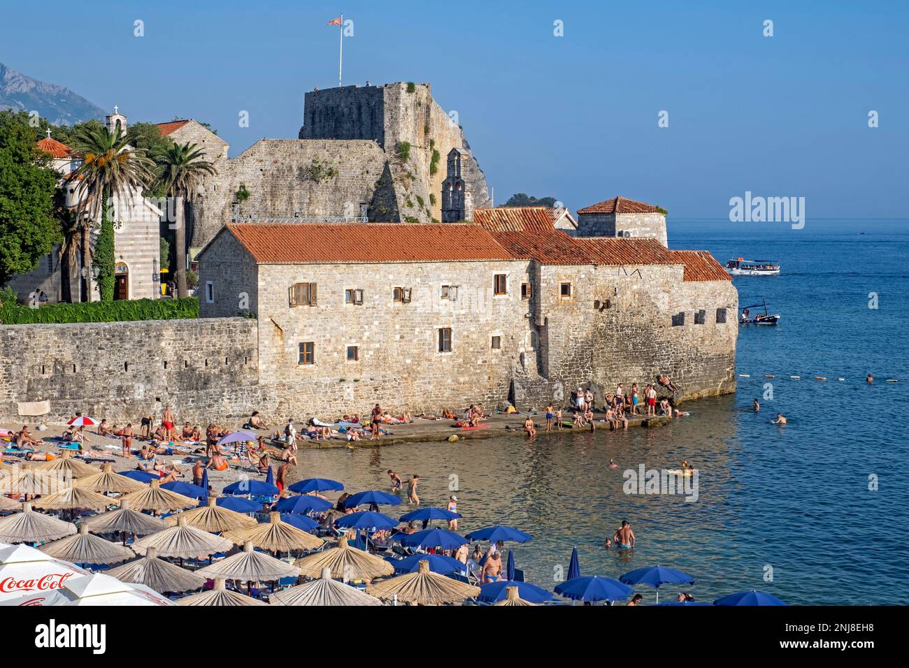 Kieselstrand mit Sonnenanbetern im Sommer außerhalb der venezianischen Stadtmauern von Budua in der mittelalterlichen Stadt Budva entlang der Adria, Montenegro Stockfoto