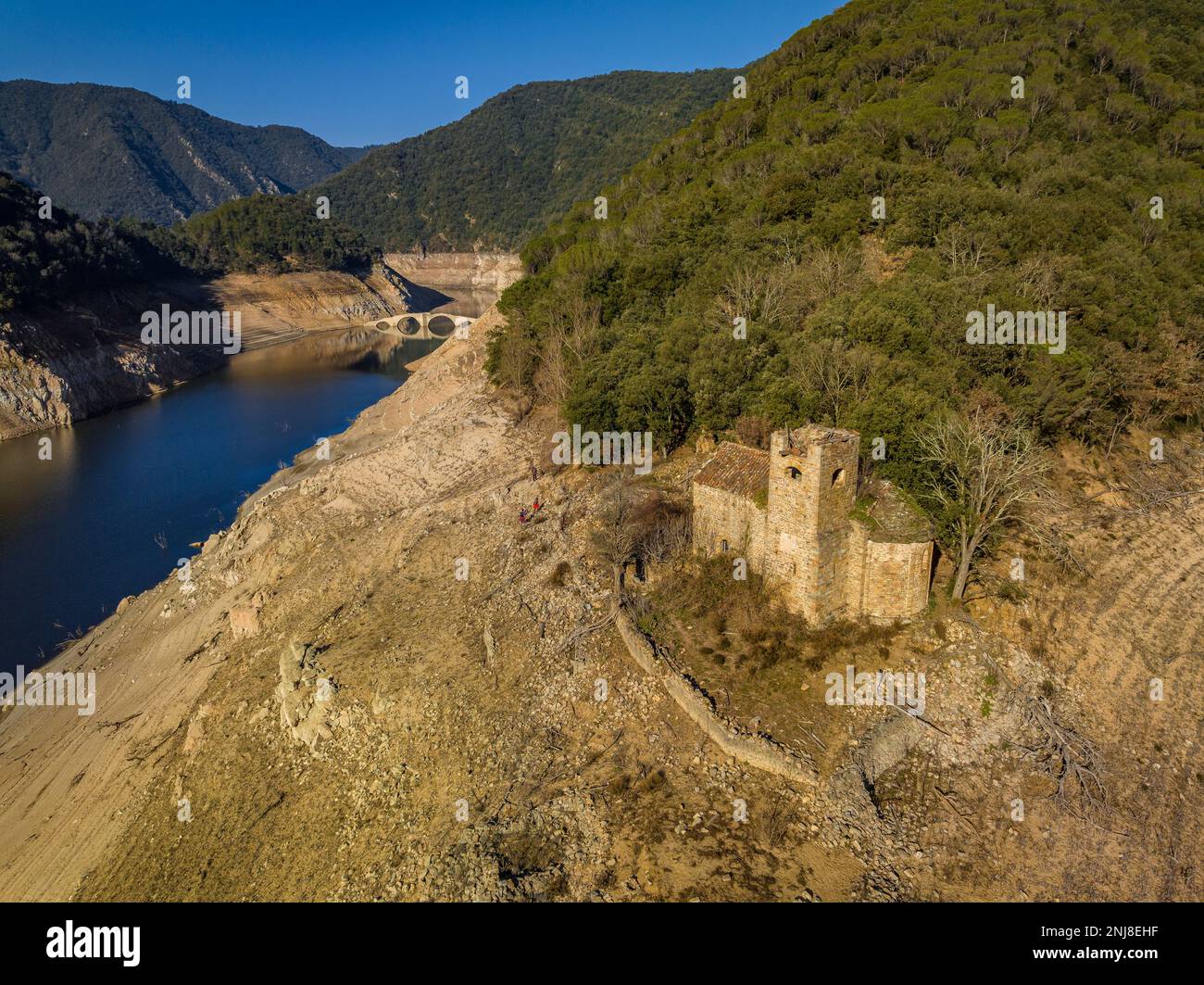 Romanische Kirche Sant Martí de Querós neben dem Wasser des Susqueda-Reservoirs. Im Hintergrund: Die Querós-Brücke, Girona, Katalonien, Spanien Stockfoto