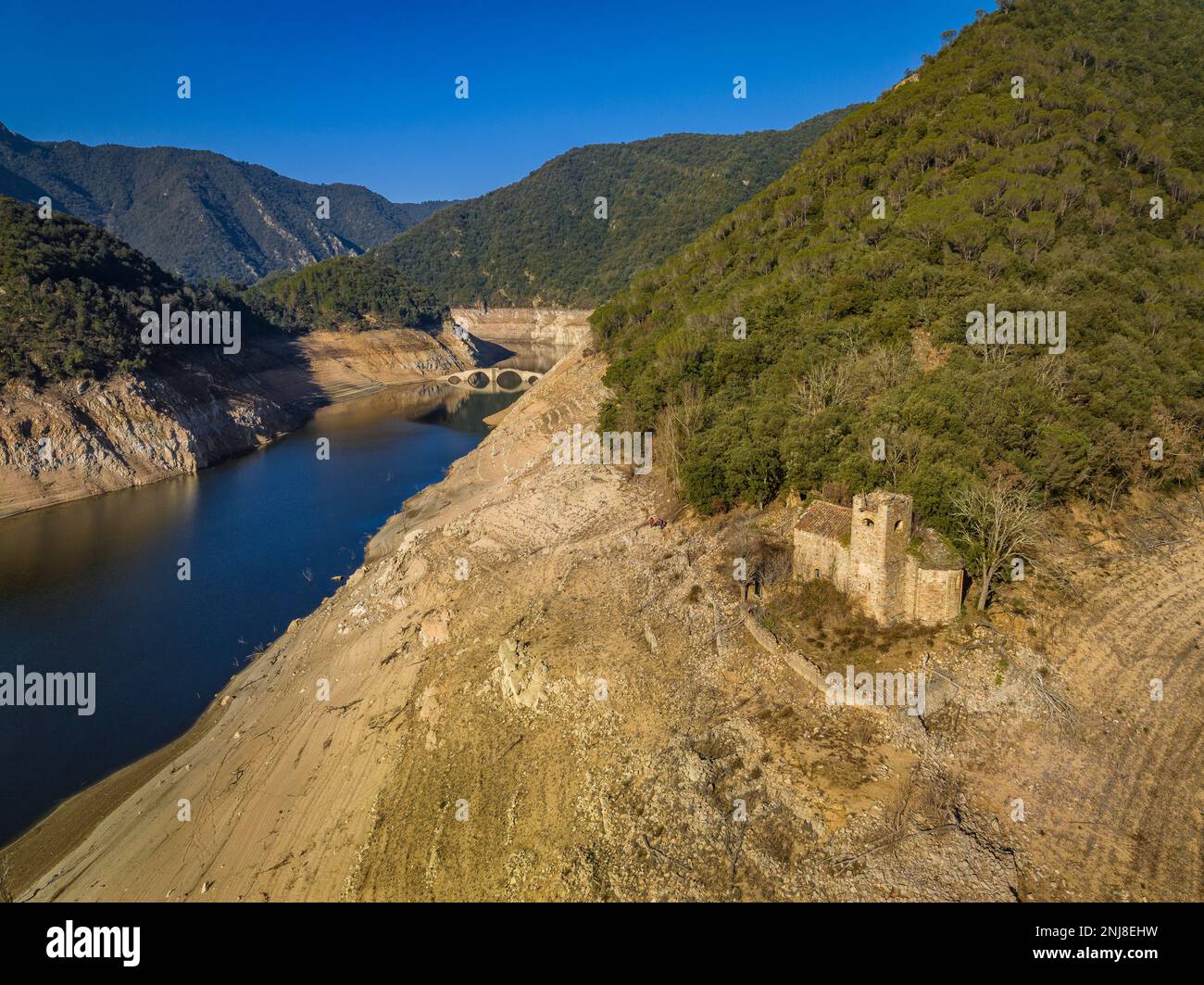 Romanische Kirche Sant Martí de Querós neben dem Wasser des Susqueda-Reservoirs. Im Hintergrund: Die Querós-Brücke, Girona, Katalonien, Spanien Stockfoto