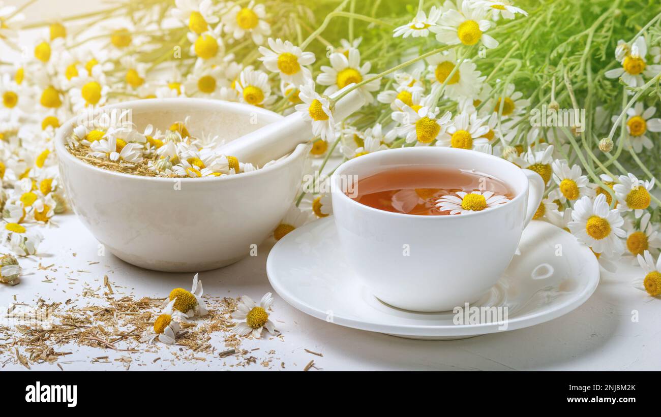 Ländliche Stillleben - Tasse gebrühten Kamillentee auf dem Hintergrund eines Straußes von Gänseblümchen, Nahaufnahme Stockfoto