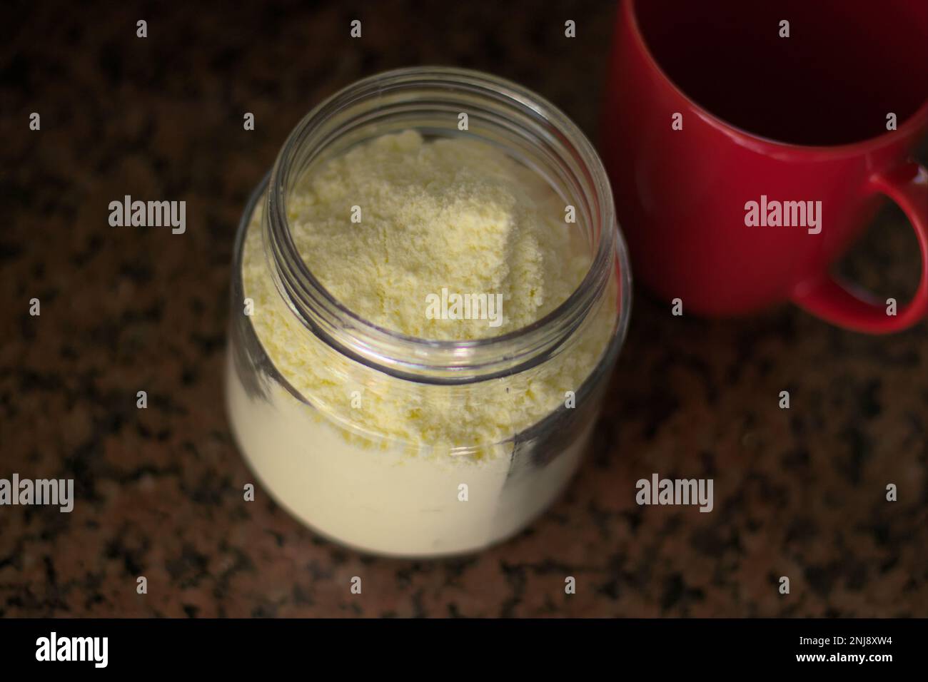 Glasbehälter mit Milchpulver und rotem Becher. Tageslicht. Stockfoto