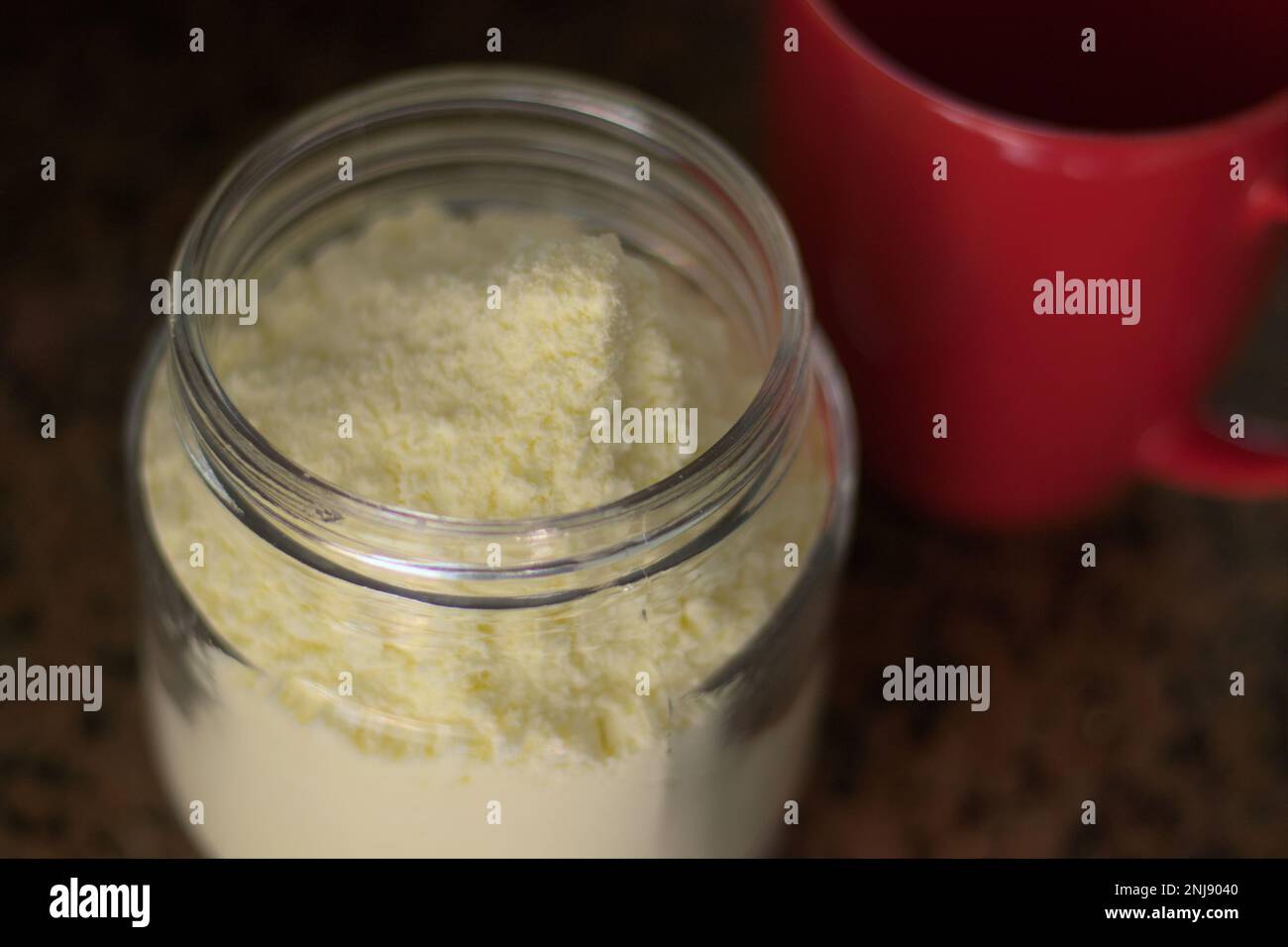Glasbehälter mit Milchpulver und rotem Becher. Tageslicht. Stockfoto