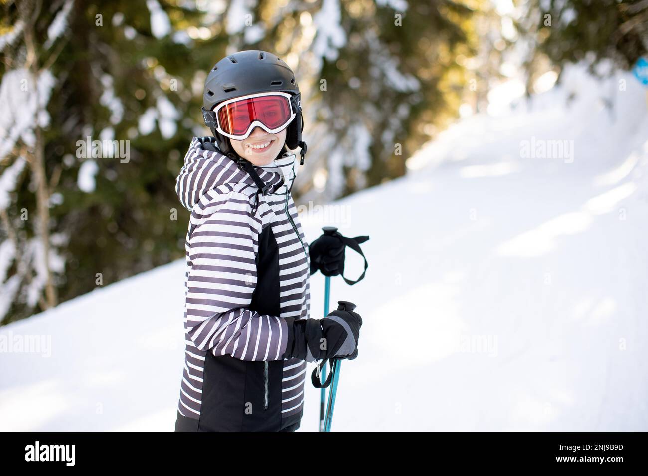 Junge Frau genießt den Wintertag beim Skifahren auf den schneebedeckten Pisten, umgeben von hohen Bäumen und kaltgekleidet Stockfoto