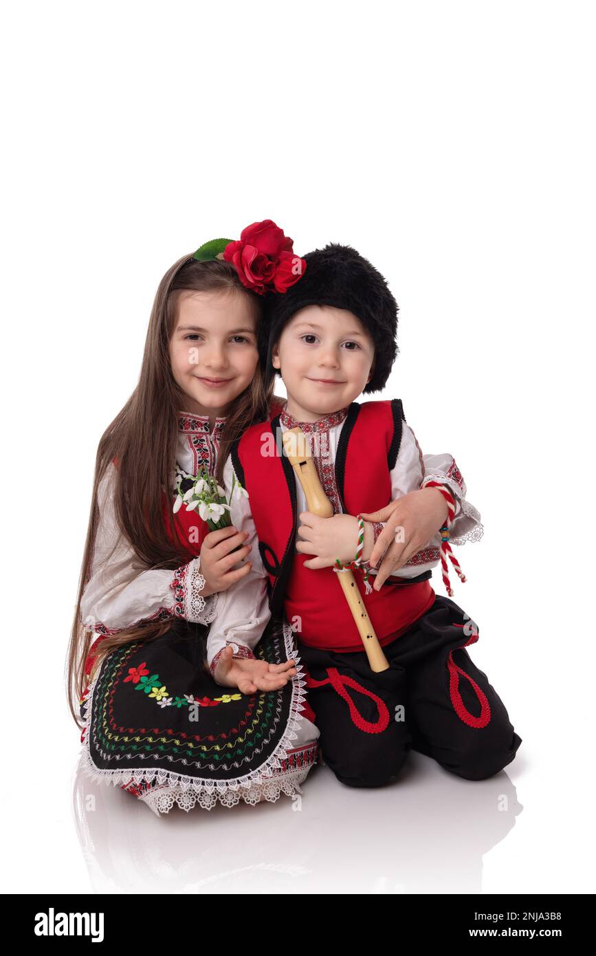 Bulgarische Kinder Jungen und Mädchen in traditionellen Folklore-Kostümen mit Frühlingsblumen, Schneetropfen und handgefertigten Wollarmband Martenitsa Symbol von Baba Marta Stockfoto