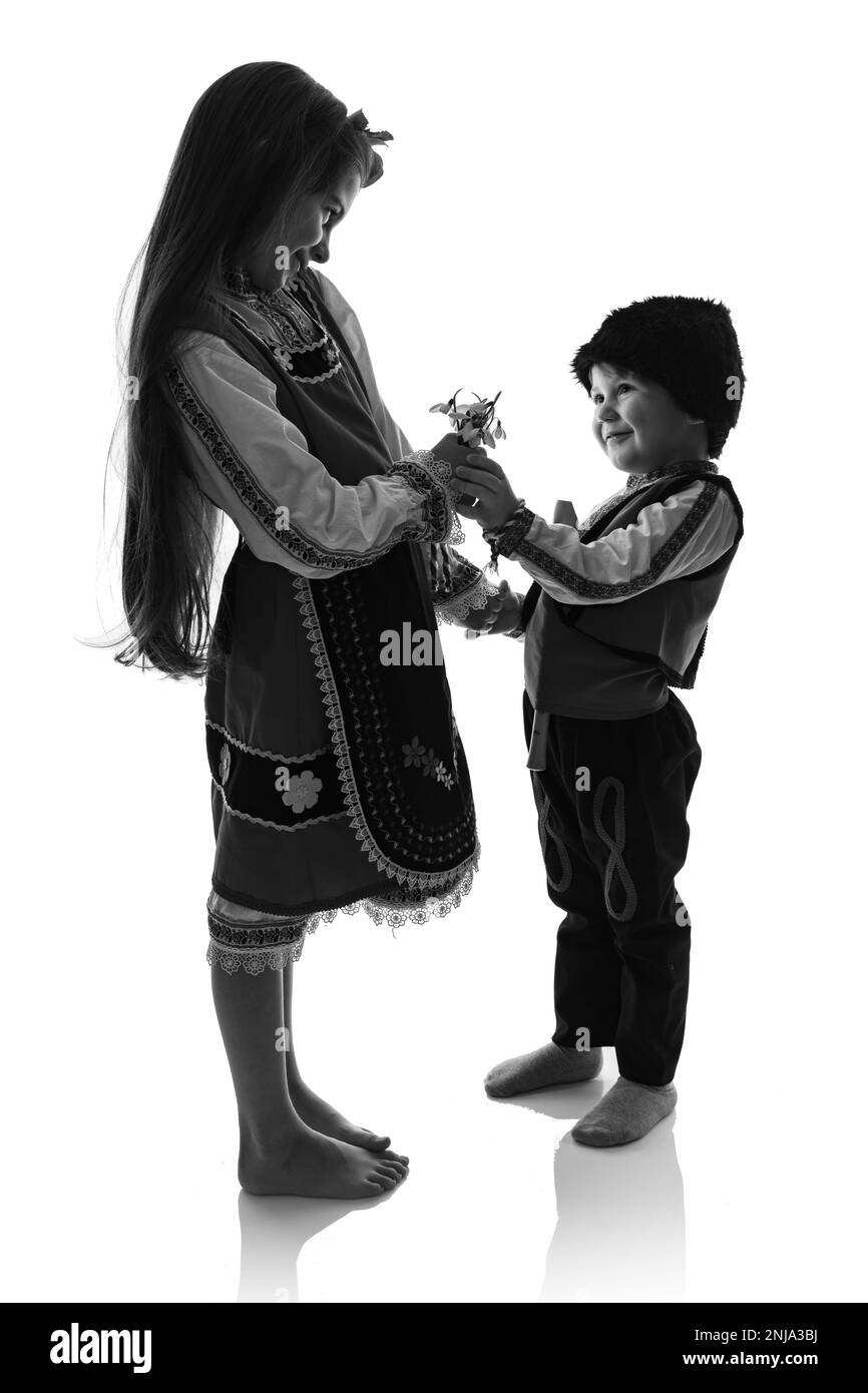Bulgarische Kinder Jungen und Mädchen in traditionellen Folklore-Kostümen mit Frühlingsblumen, Schneetropfen und handgefertigten Wollarmband Martenitsa Symbol von Baba Marta Stockfoto
