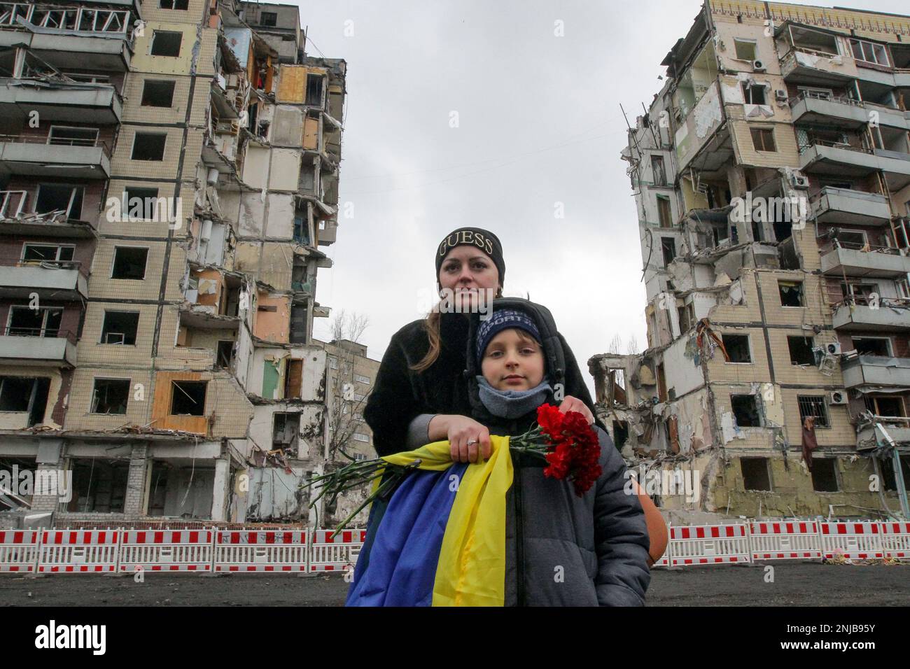 DNIPRO, UKRAINE - 22. FEBRUAR 2023 - Eine Frau mit einer ukrainischen Flagge und einem Haufen roter Nelken steht hinter einem Jungen während der Gedenkfeier o Stockfoto