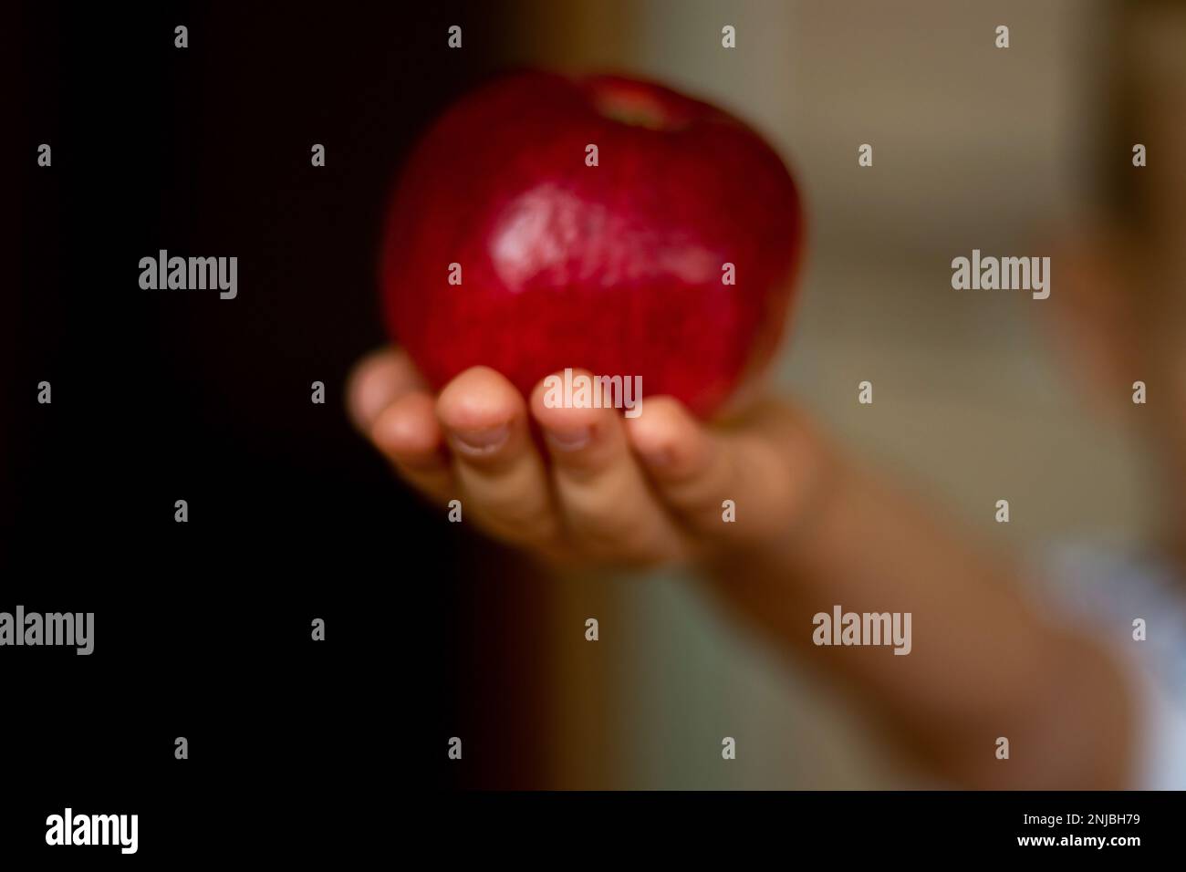 Der kleine Junge hielt seine Hand mit einem roten Apfel auf einem verschwommenen Hintergrund aus Stockfoto