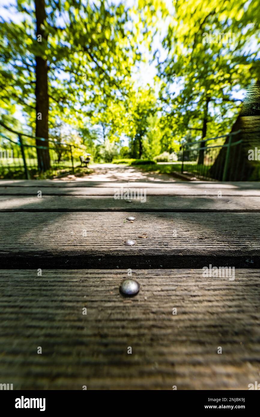 Alte renovierte Retro-Brücke mit grünen Metallgeländern über einen kleinen Fluss in einem kleinen bunten Park am sonnigen Morgen Stockfoto