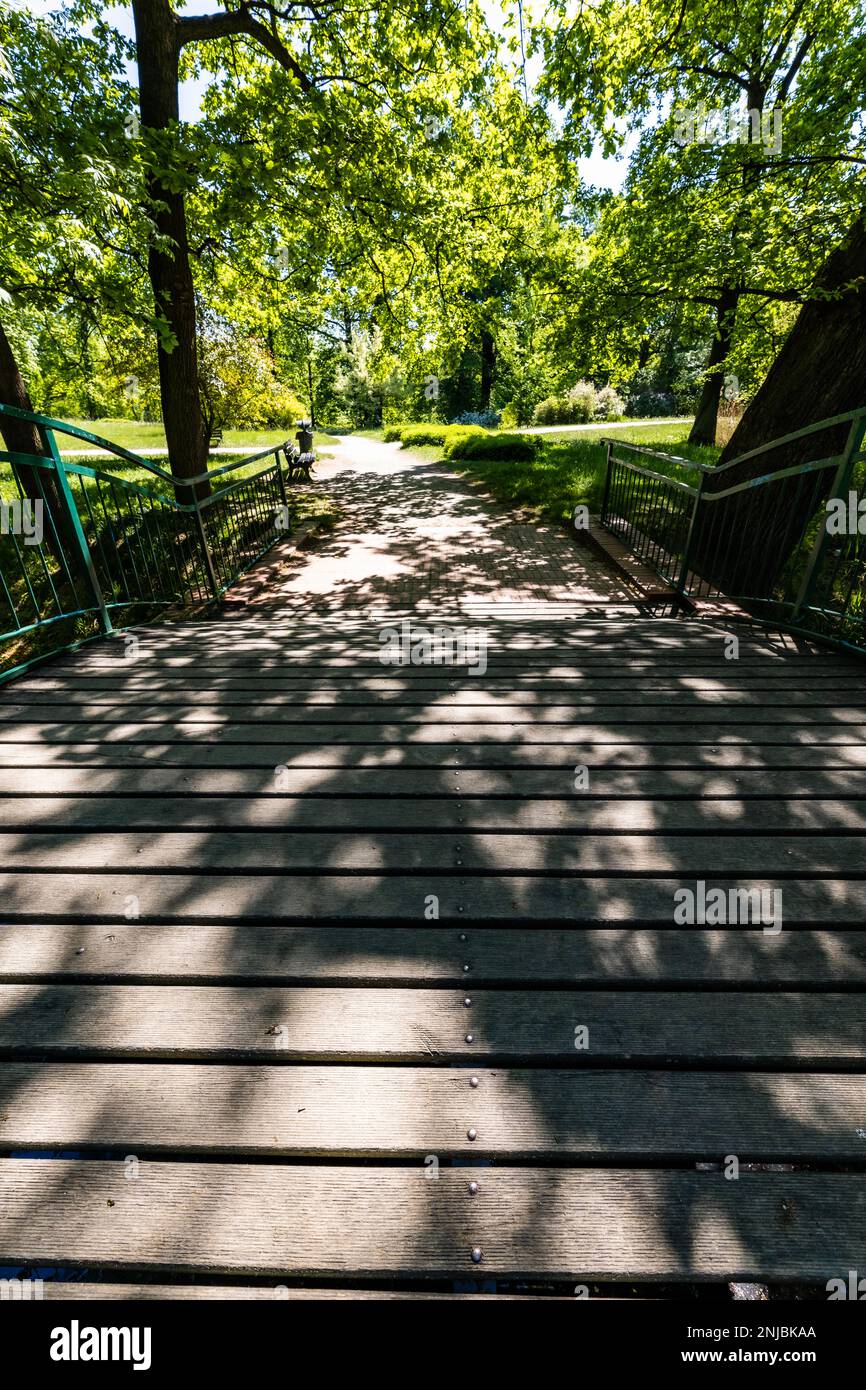 Alte renovierte Retro-Brücke mit grünen Metallgeländern über einen kleinen Fluss in einem kleinen bunten Park am sonnigen Morgen Stockfoto