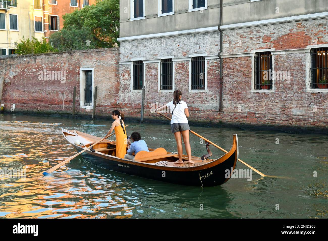 Zwei junge Frauen rudern im venezianischen Reihenstil am Rio della Misericordia-Kanal bei Sonnenuntergang, Sestiere von Cannaregio, Venedig, Italien Stockfoto