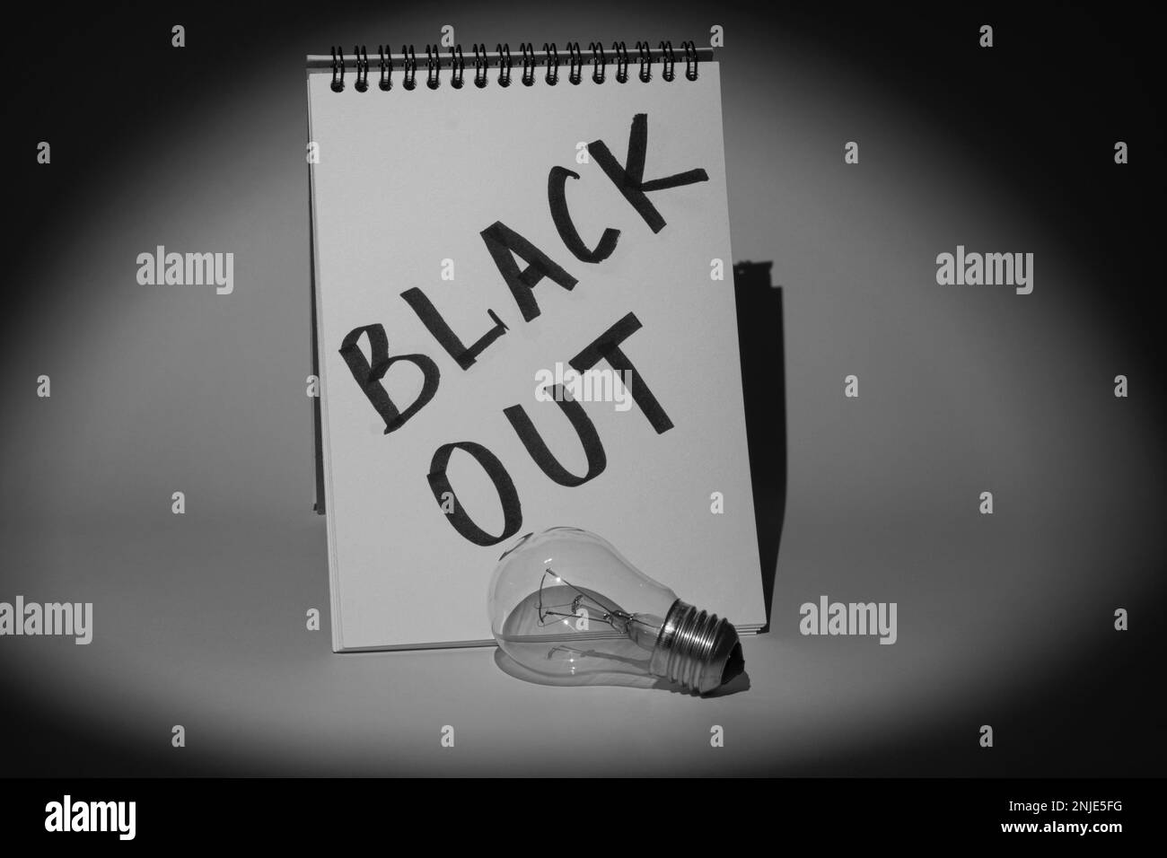 Notizblock mit der Aufschrift „Blackout“ und einer elektrischen Glühbirne, die von einem Scheinwerfer beleuchtet wird. Schwarzweißbild. Stromausfallkonzept Stockfoto