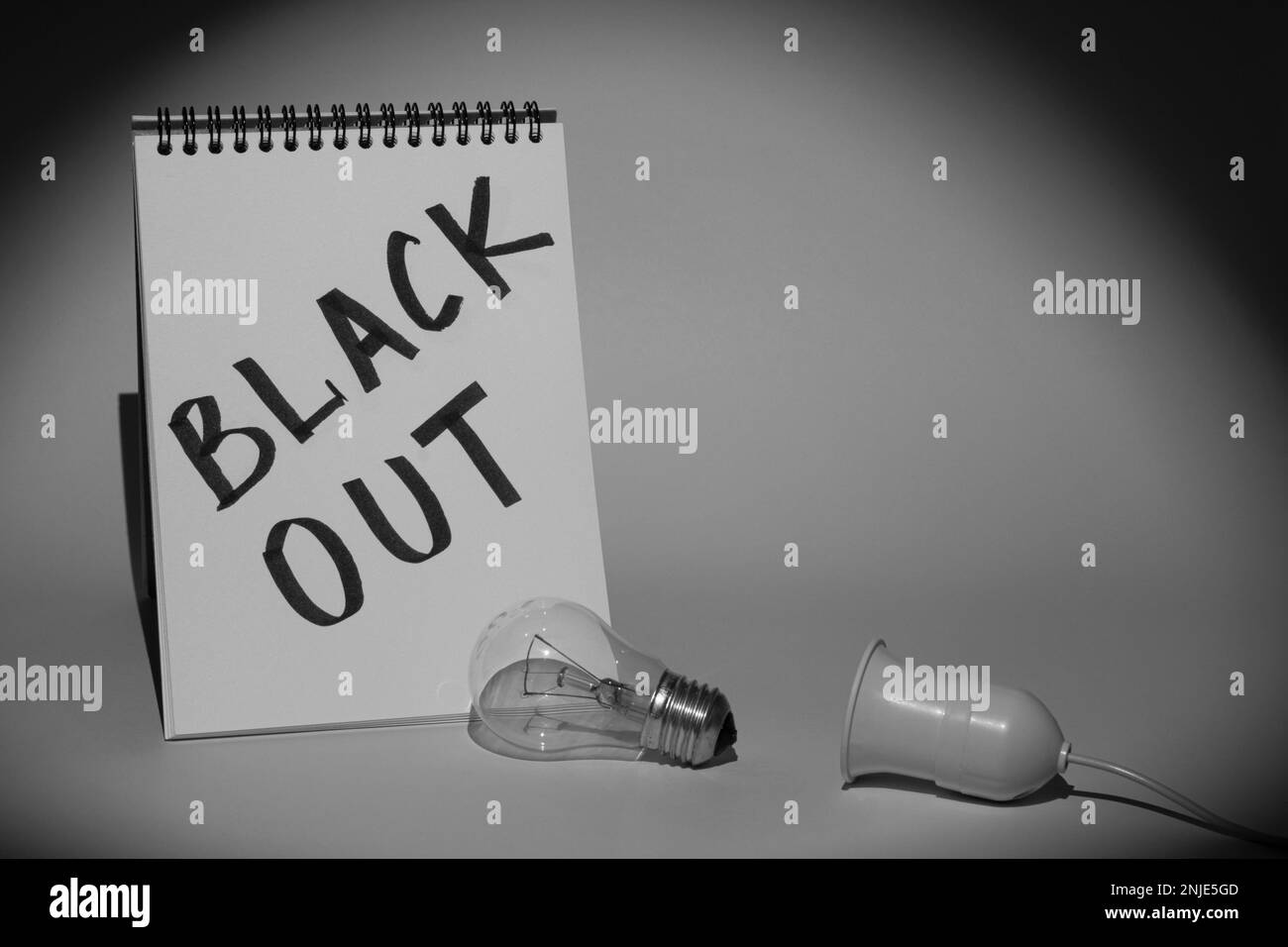Notebook mit der Aufschrift „Blackout“ und einer elektrischen Glühlampe mit einer Halterung, die von einer Taschenlampe beleuchtet wird. Schwarzweißbild Stockfoto