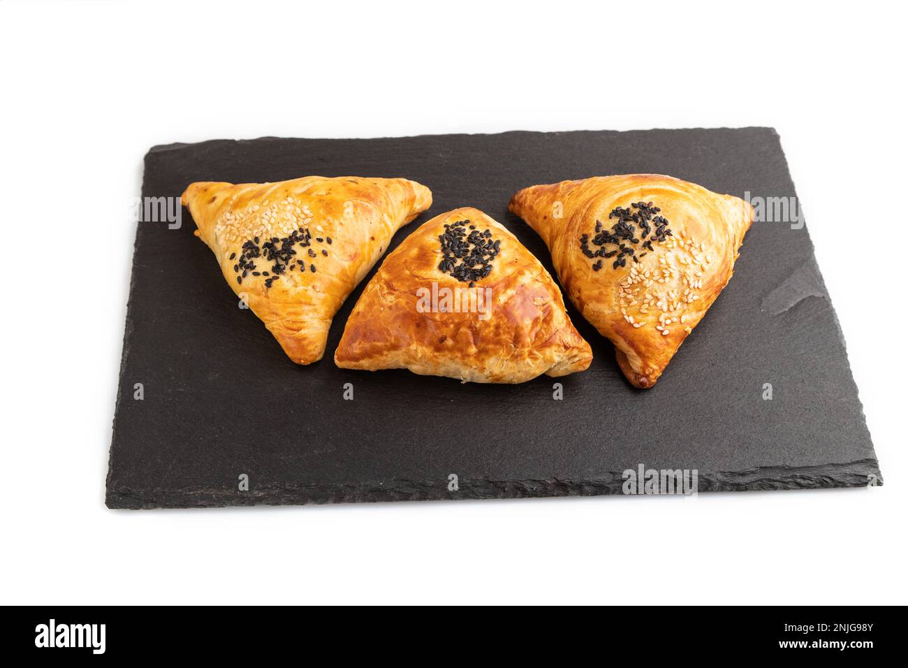 Hausgemachtes asiatisches Gebäck samosa auf schwarzem Schieferbrett isoliert auf weißem Hintergrund. Seitenansicht, Nahaufnahme. Stockfoto