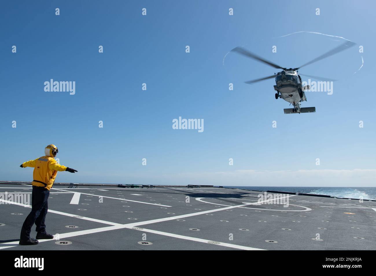 230218-N-MK318-1213 OSTPAZIFIK (18. Feb. 2023) Boatswain's Mate 2. Klasse Sam Peterson, ein blauer Matrose an Bord des Kampfschiffs USS Mobile (LCS 26) der Independence-Variante, signalisiert einem MH-60R Hubschrauber, der am Helicopter Maritime Strike Squadron 49 (HSM 49) befestigt ist, vom Cockdeck des Schiffes abzuheben, Feb. 18. Küstenschiffe sind schnelle, optimal bemannte, auf die Mission zugeschnittene Surface Combatants, die in küstennahen und offenen Meeresumgebungen operieren und gegen die Bedrohungen der Küste des 21. Jahrhunderts gewinnen. Mobile führt derzeit Routinevorgänge in der US-3.-Flotte durch. ( Stockfoto