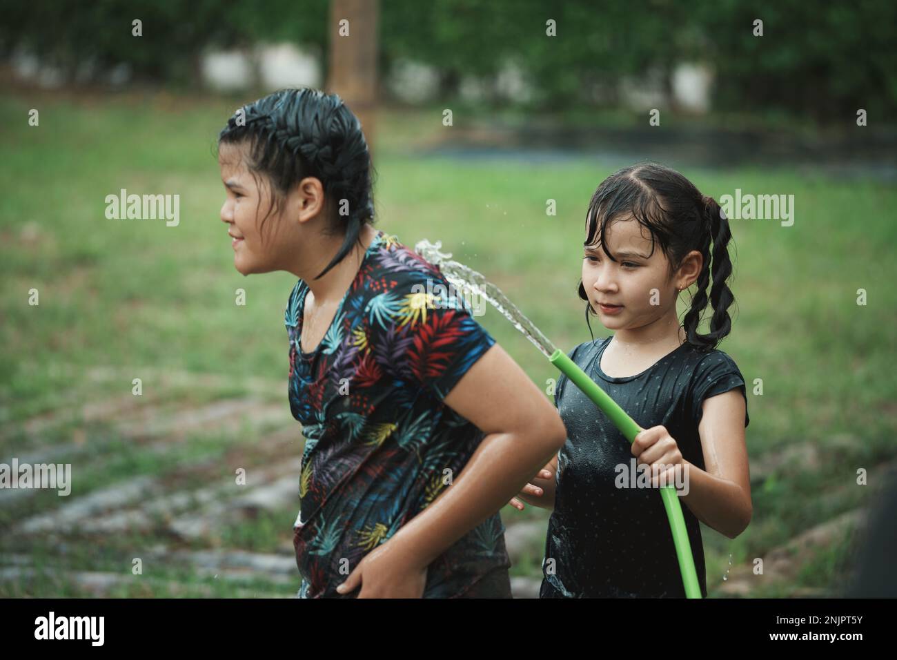 Das Mädchen mit zwei Kindern hat Spaß beim Spielen im Wasser von der Wasserleitung im Freien. Ein Mädchen, das Schlamm von Wasser aus dem Schlauch entfernt hat. Stockfoto