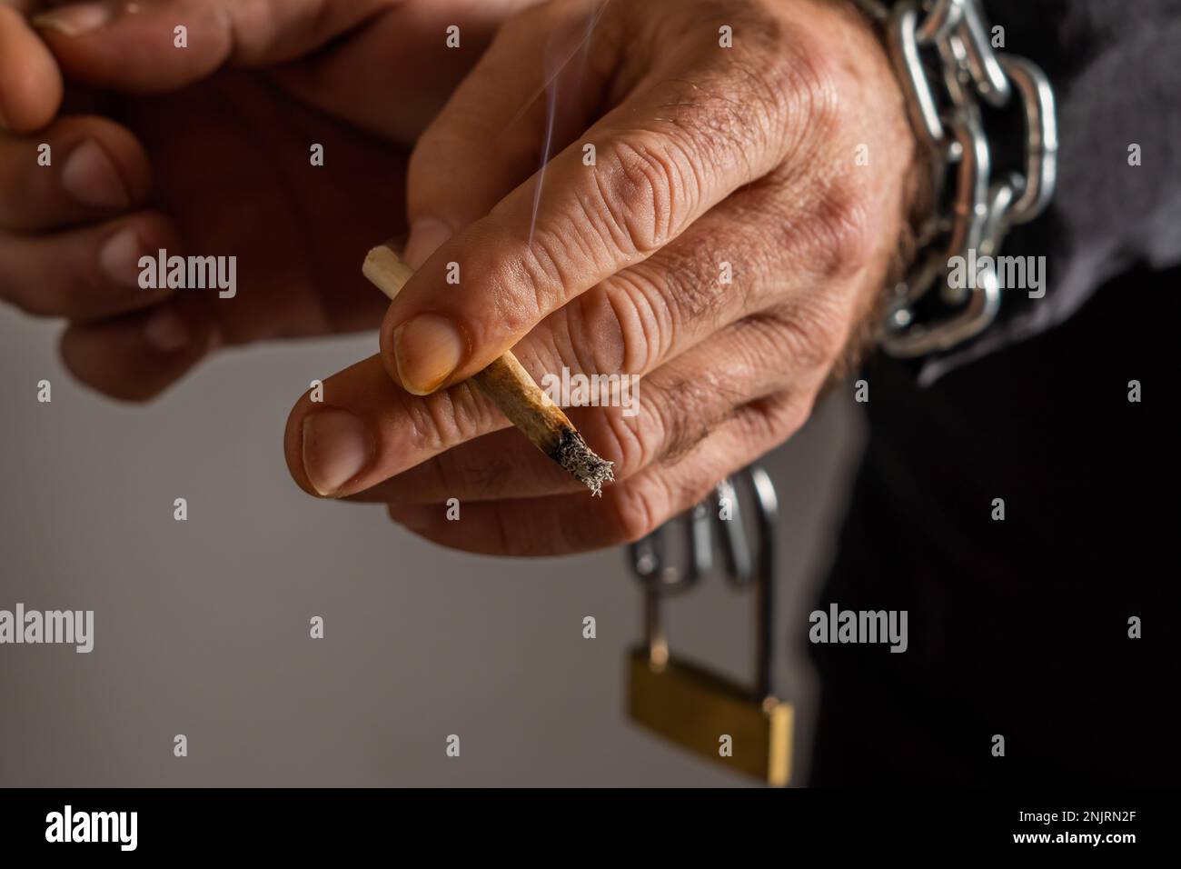 Die Hände des Mannes sind angekettet, mit einer Zigarette in den Fingern, schwarzer Hintergrund, Suchtbegriff Stockfoto