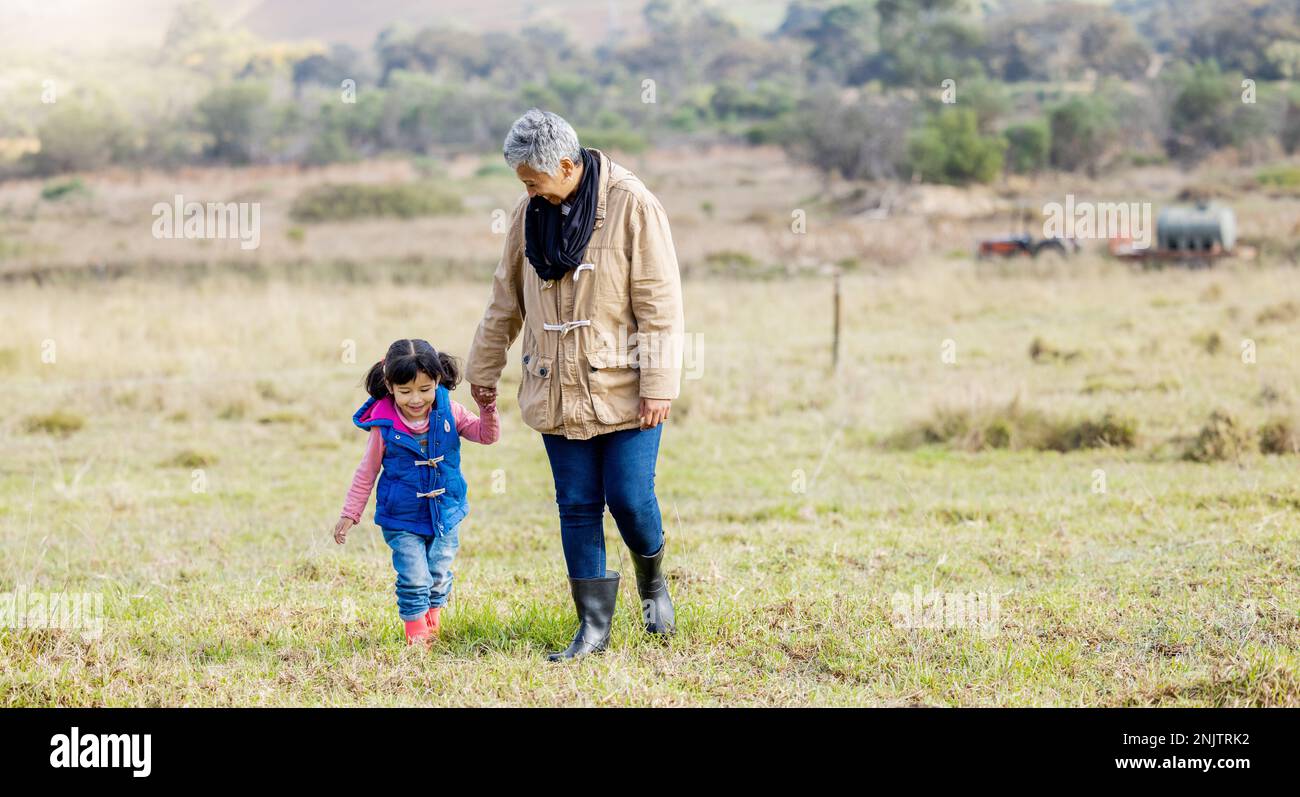 Oma, Mädchen und Händchen halten für einen Spaziergang auf Gras, eine Familienfarm und eine Beziehung mit Liebe im Freien. Alte Frau, Kind und helfende Hand in Hand Stockfoto