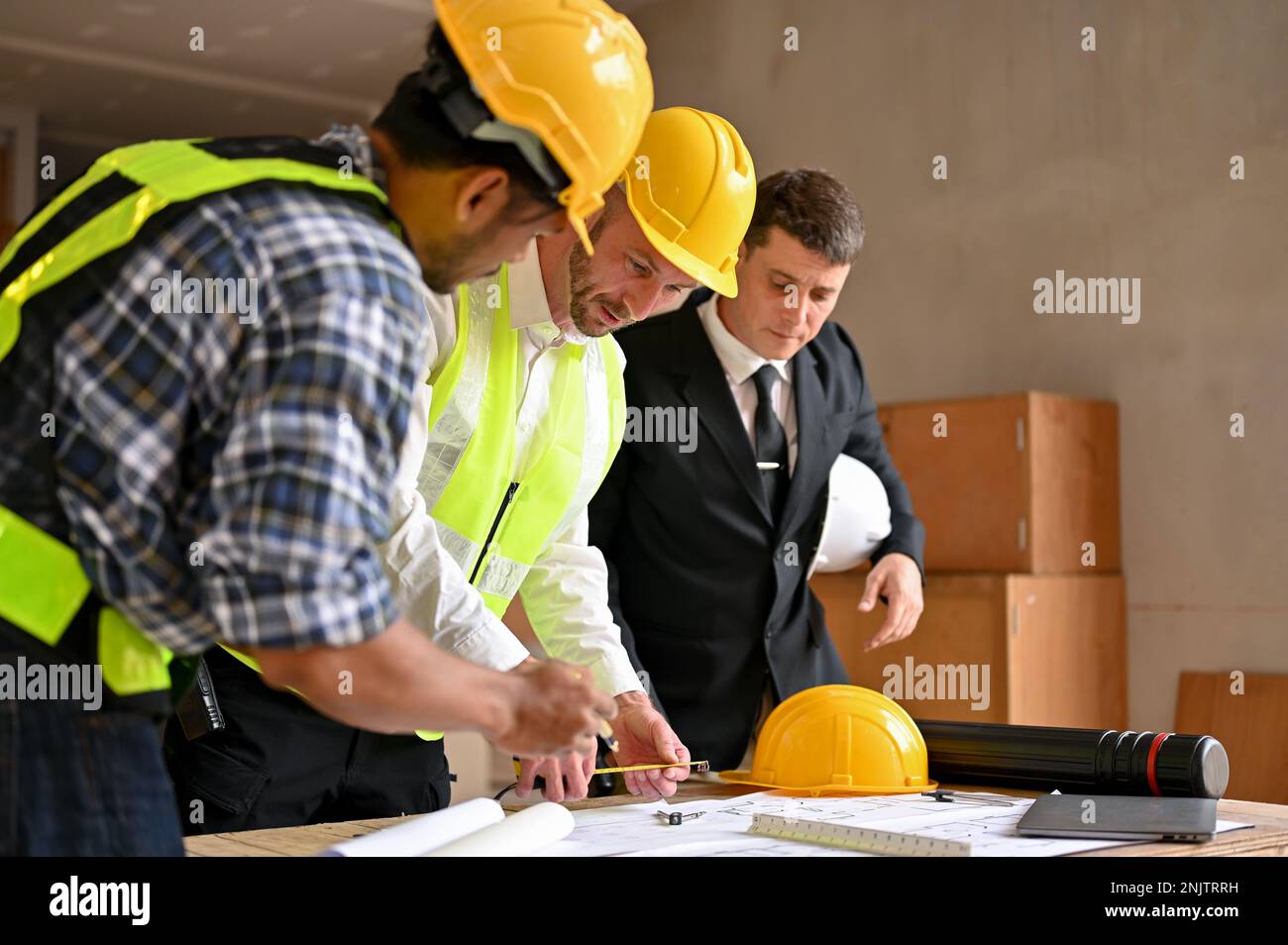 Ein professioneller weißer Bauingenieur, der einem asiatischen männlichen Inspektor und Cauc den Bauprozess und die Skalierung auf dem Bauplan erläutert Stockfoto