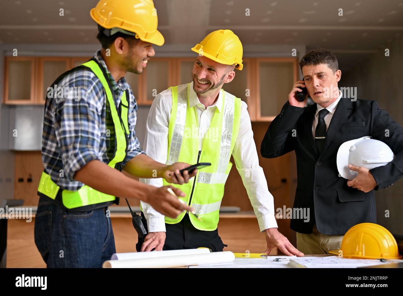 Professioneller, männlicher Bauingenieur, der mit einem asiatischen Bauinspektor spricht und den Bauprozess plant, während er Kauz ist Stockfoto