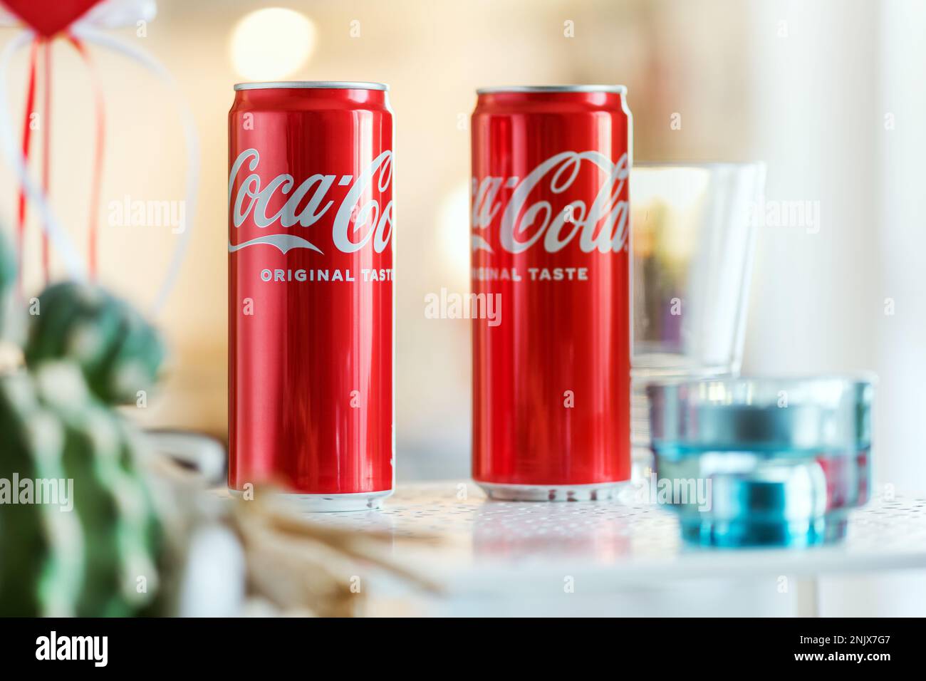 Coca-Cola-Dosen werden auf dem Tisch neben Glas vor einem verschwommenen Hintergrund einer leichten Küche platziert Stockfoto