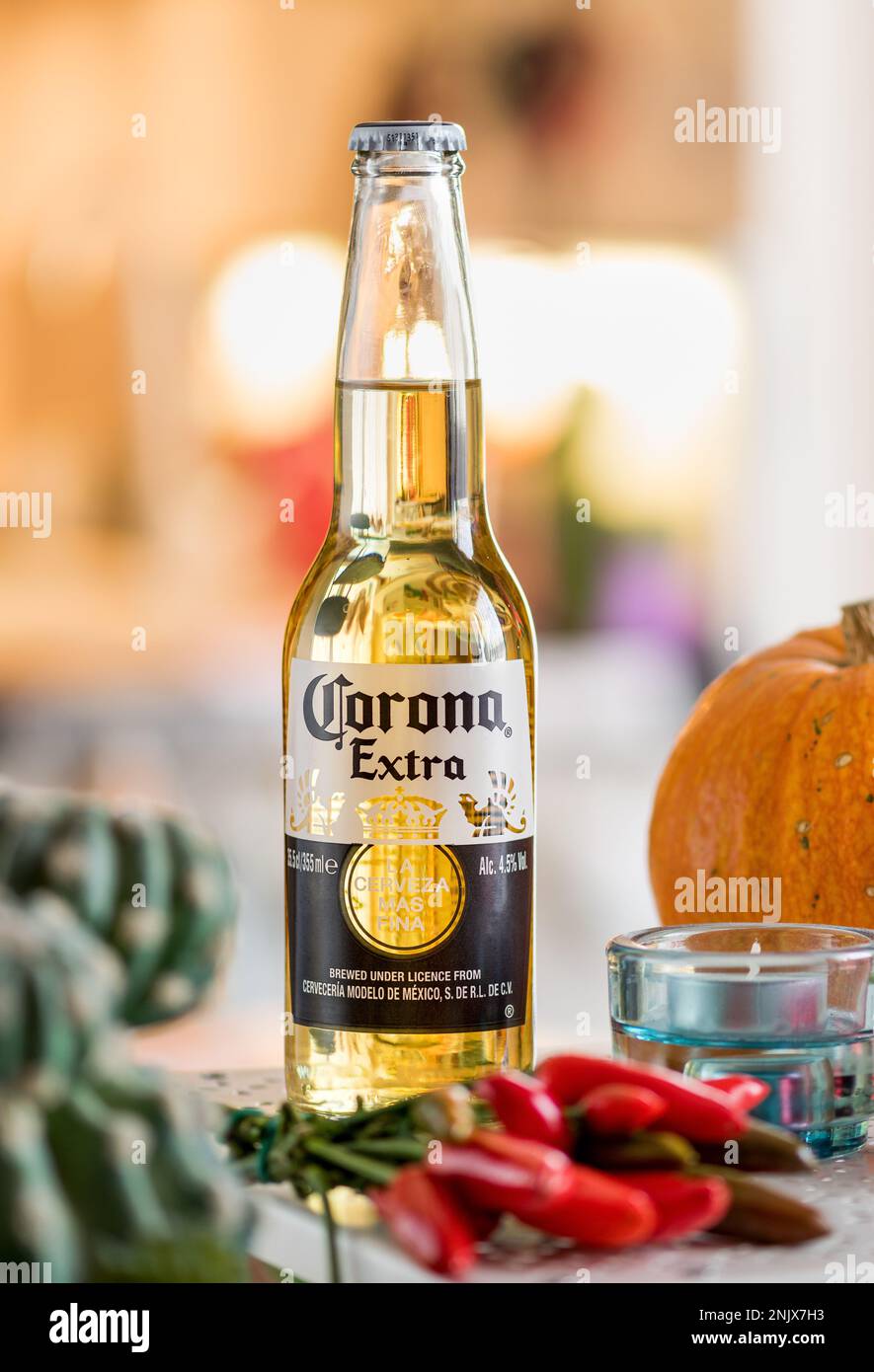 Glasflasche Corona Extra Bier auf dem Tisch neben Kürbis und roten Paprika vor verschwommenem Hintergrund Stockfoto