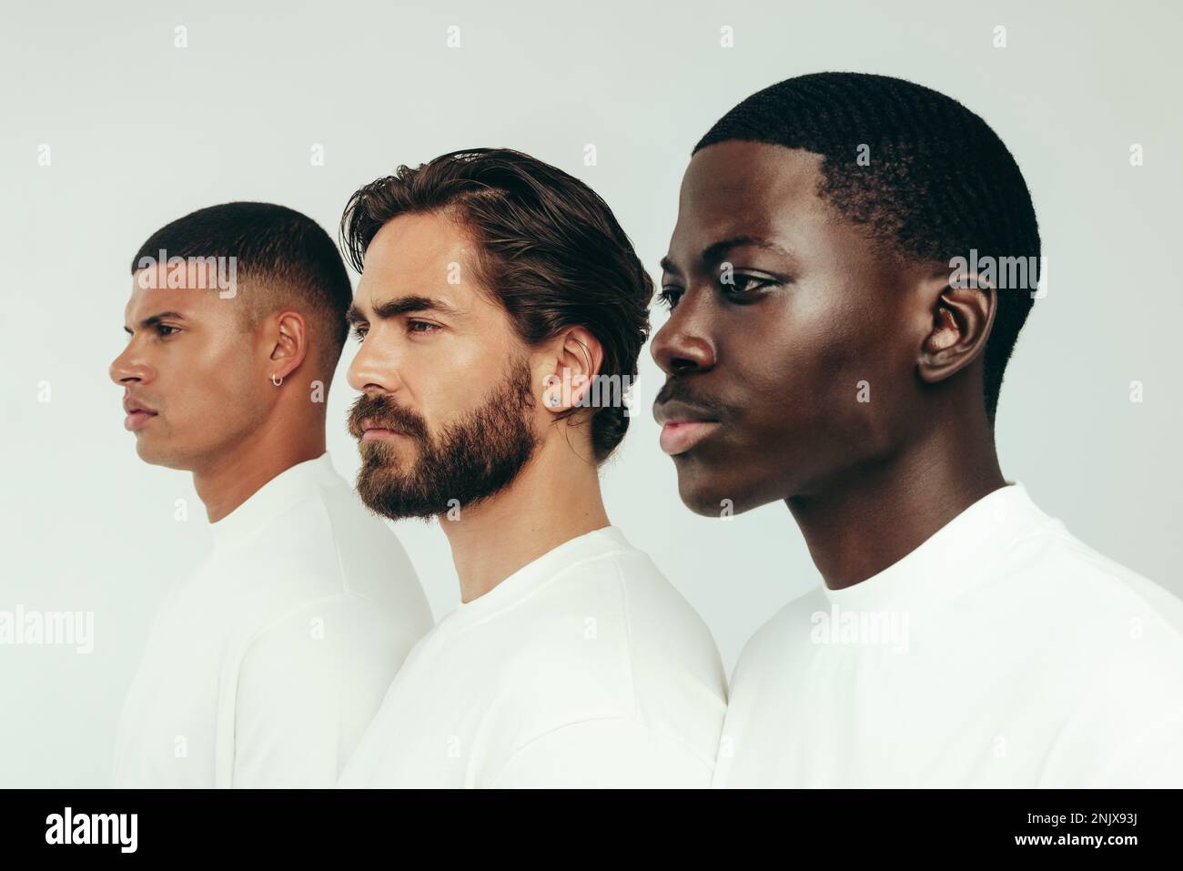 Männer zeigen Selbstvertrauen und Schönheit, während sie in einem Studio zusammenstehen. Drei junge Männer, jeder mit einem einzigartigen Hautton, zeigen die makellosen Ergebnisse von s. Stockfoto