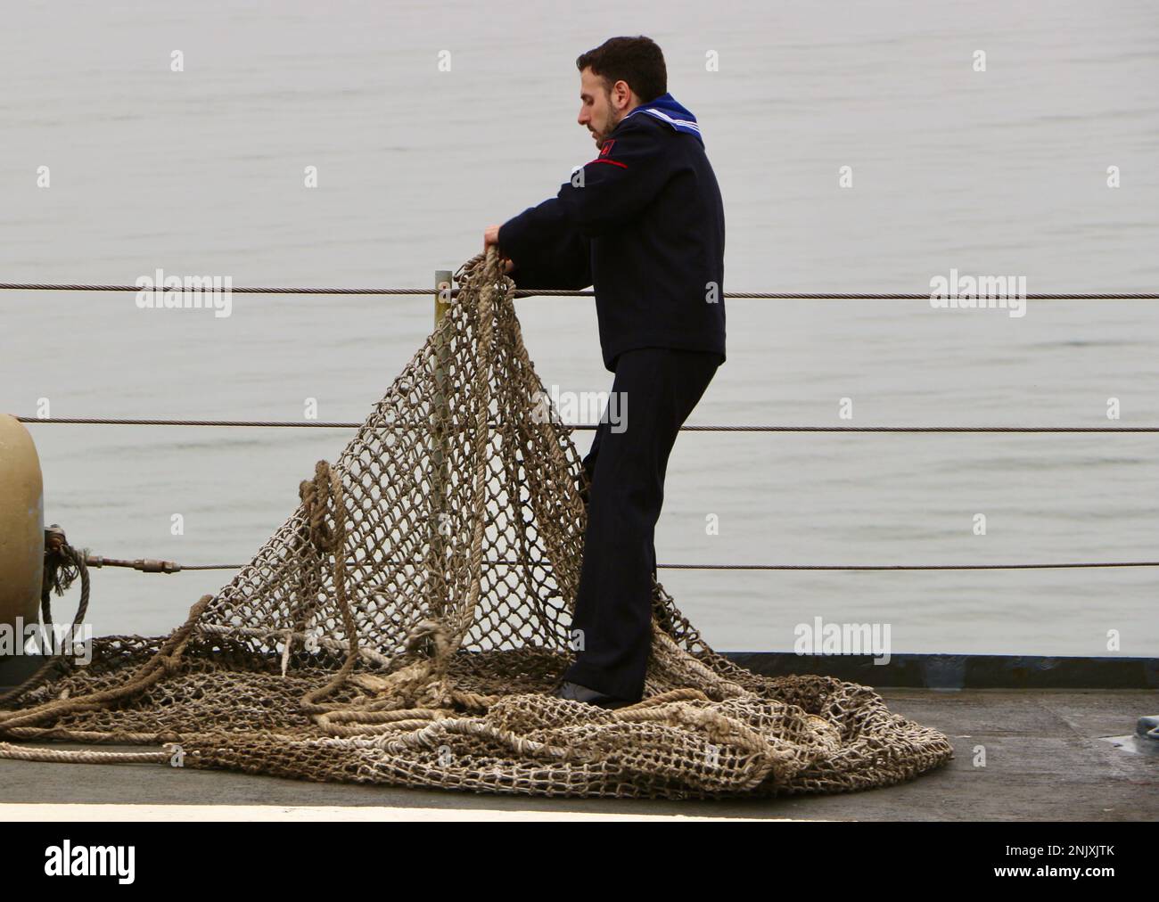 Ein spanischer Seemann mit Netz, der sich auf einen Tag der offenen Tür an Bord des Serviola P-71 Patrouillenboots vorbereitet, das in Gamazo Santander Kantabrien Spanien vor Anker liegt Stockfoto