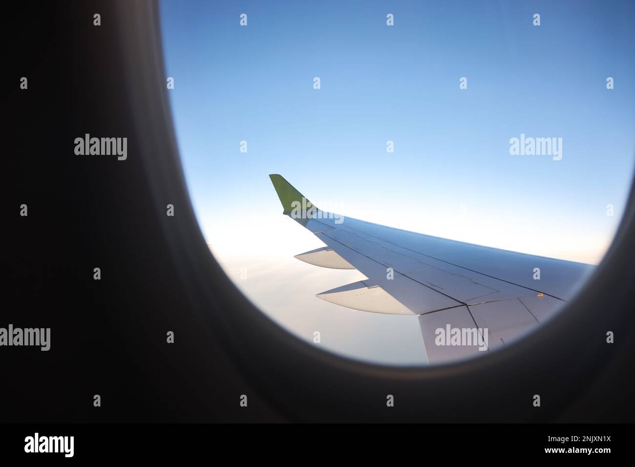 Dieses atemberaubende Stockfoto zeigt die Aussicht aus einem Fenster eines Passagierflugzeugs und zeigt einen majestätischen Flügel, der durch den klaren, wolkenlosen Himmel schwebt Stockfoto