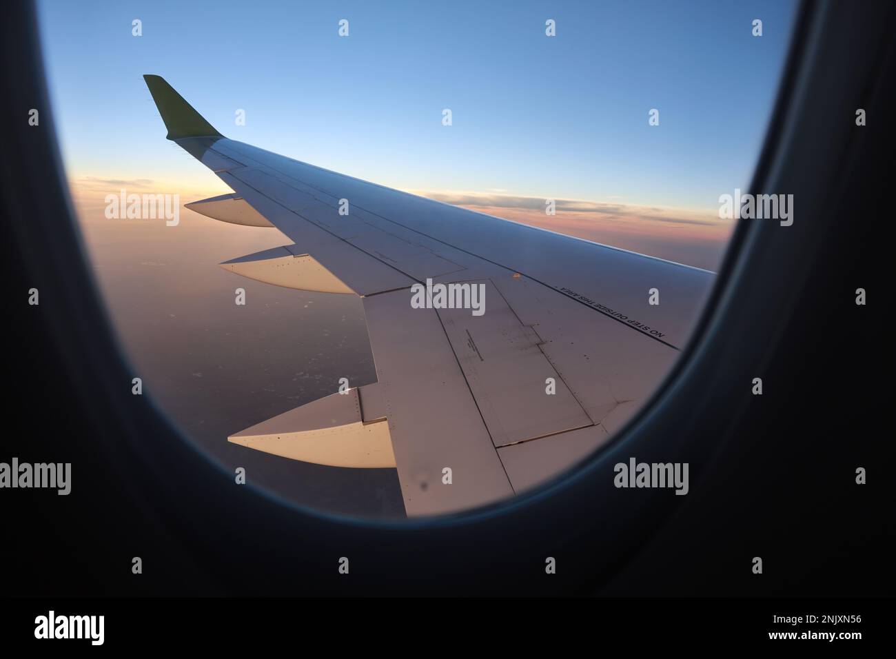 Dieses atemberaubende Stockfoto zeigt die Aussicht aus einem Fenster eines Passagierflugzeugs und zeigt einen majestätischen Flügel, der durch den klaren, wolkenlosen Himmel schwebt Stockfoto