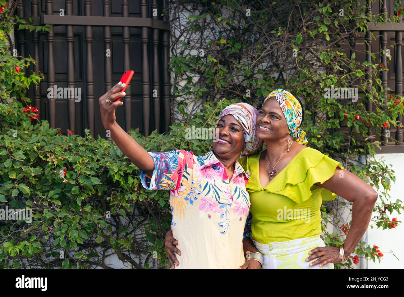 Lächelnde, ethnische Freundinnen in Sommerkleidung und Kopftuch Selfie auf dem Handy während eines Wochenendes in der Stadt Stockfoto