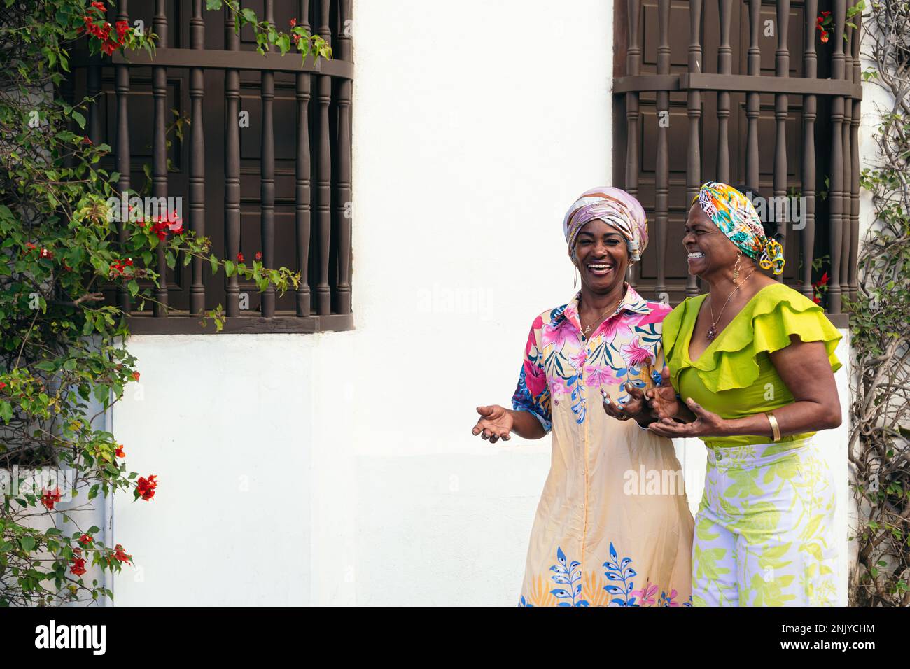 Alte hispanische Freundinnen in bunten Outfits und Accessoires spazieren auf der Straße der Stadt, während sie sich unterhalten Stockfoto